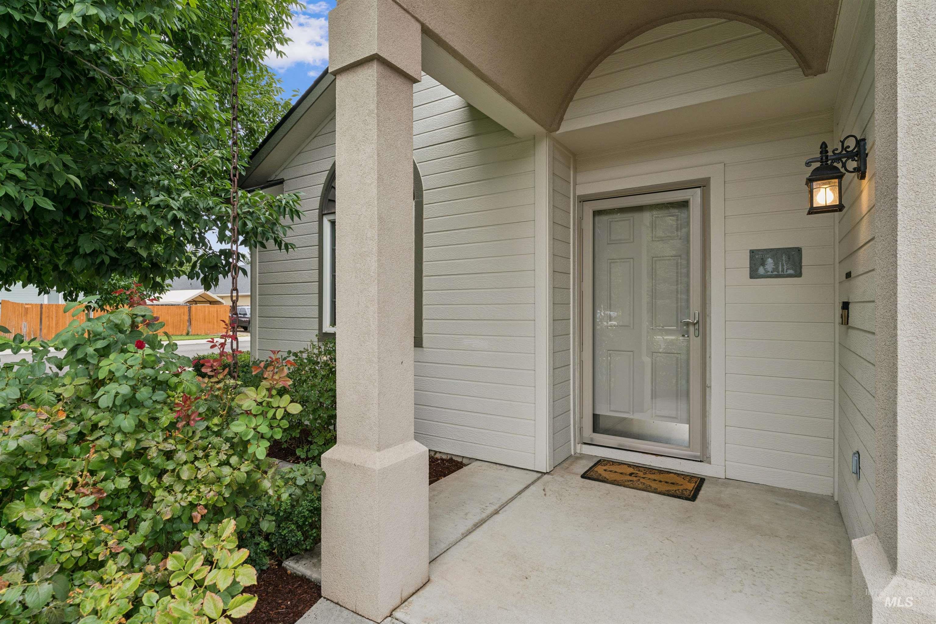 Covered home entrance with a gray glass-paneled door, arched porch ceiling, and leafy rose garden.