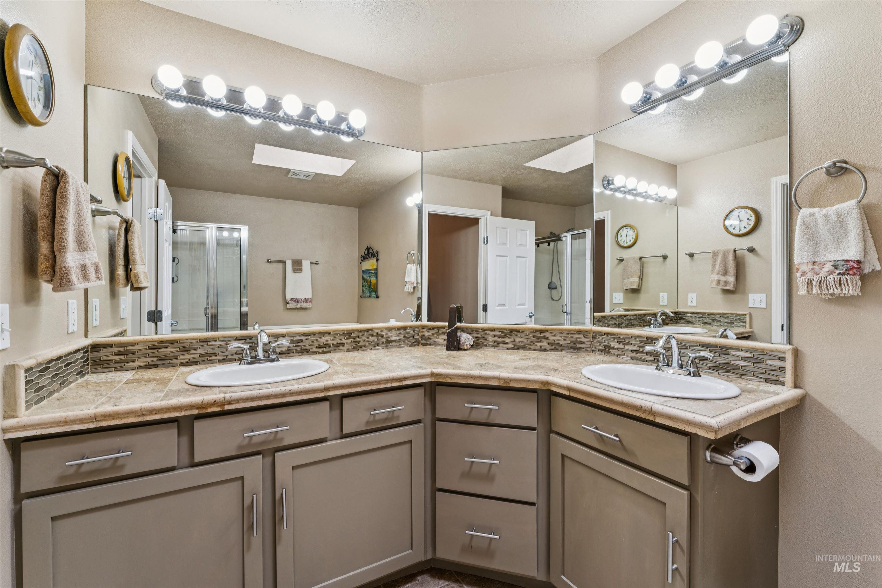 Bathroom vanity with two sinks, extensive mirrors, bright lights, and a glass-enclosed shower.