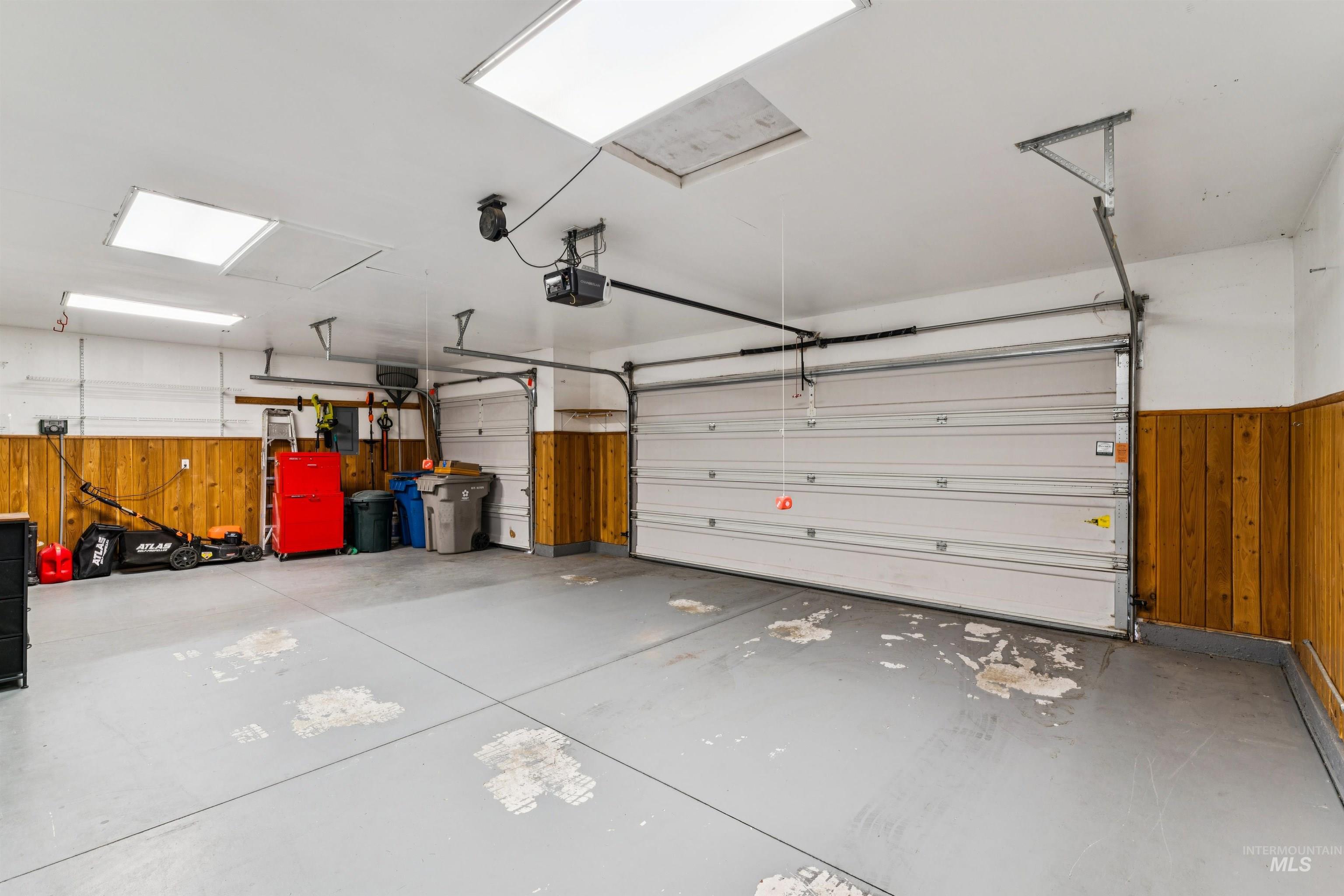 Two-car garage with white overhead doors, wood-paneled walls, and stored tools along one side.