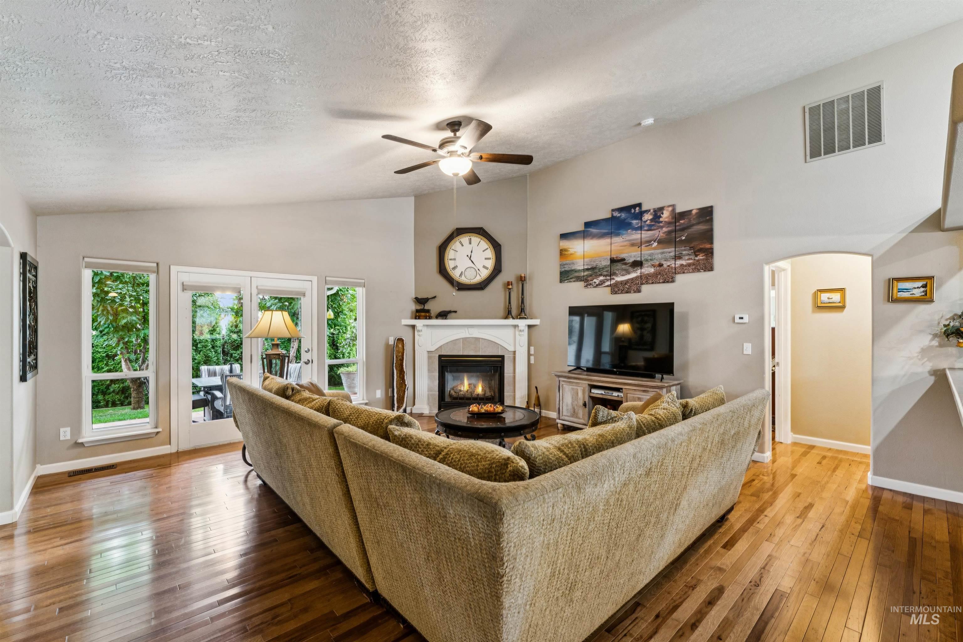 Living room with a large sectional, fireplace, hardwood floors, and glass doors opening toward greenery.
