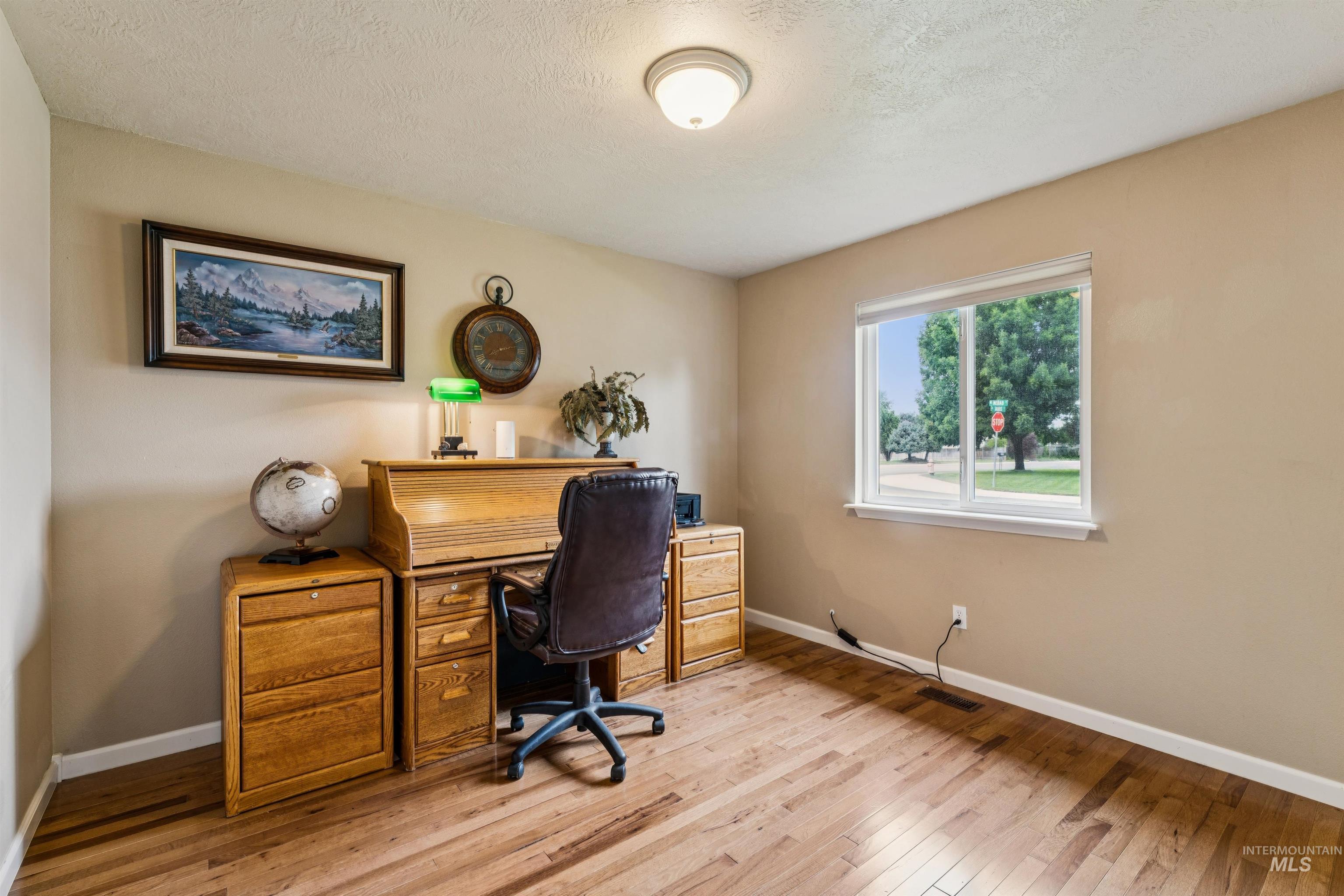 Furnished home office with a wooden roll-top desk, leather chair, and hardwood floors.