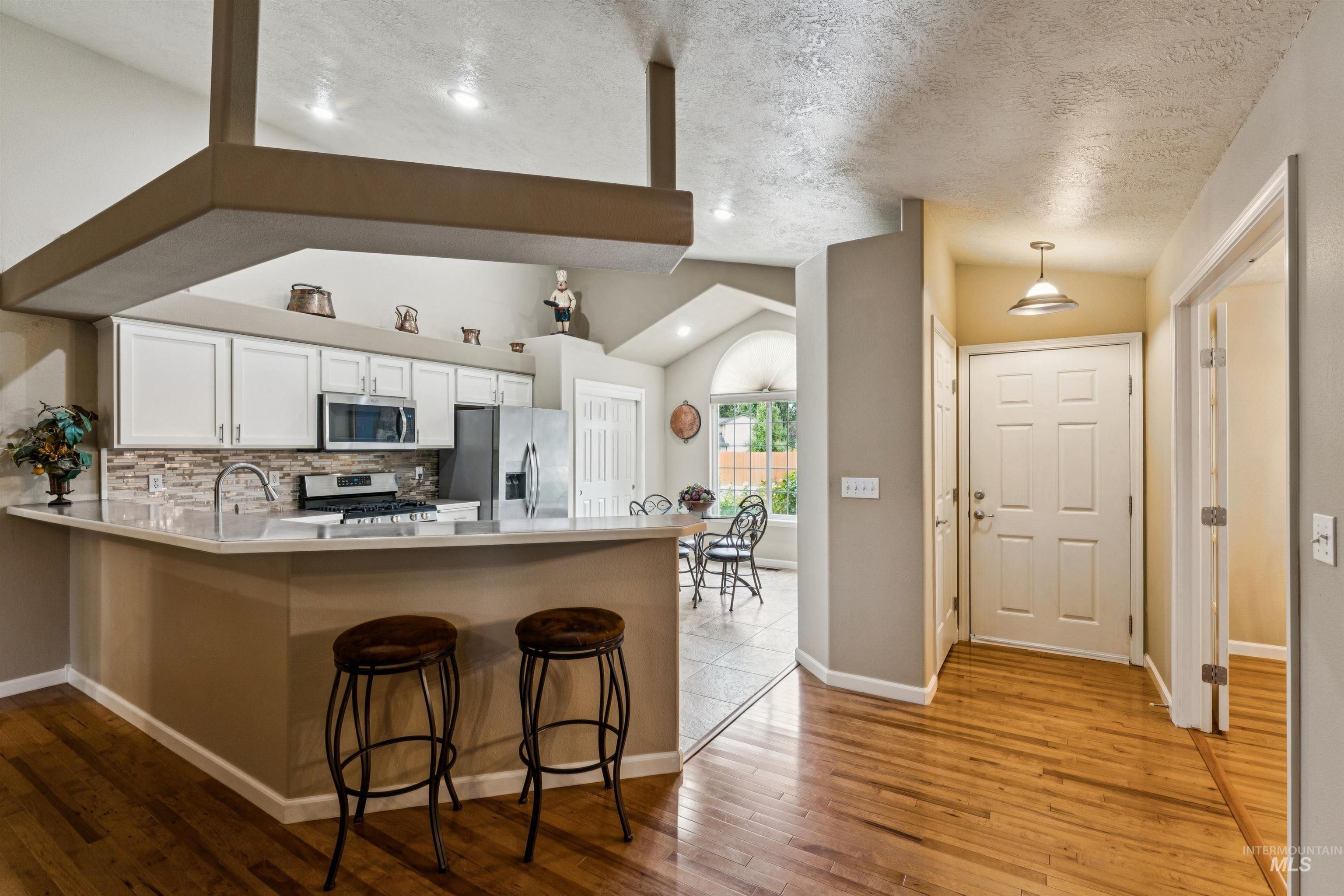 Kitchen with white cabinets, stainless appliances, and a breakfast bar beside the entryway.