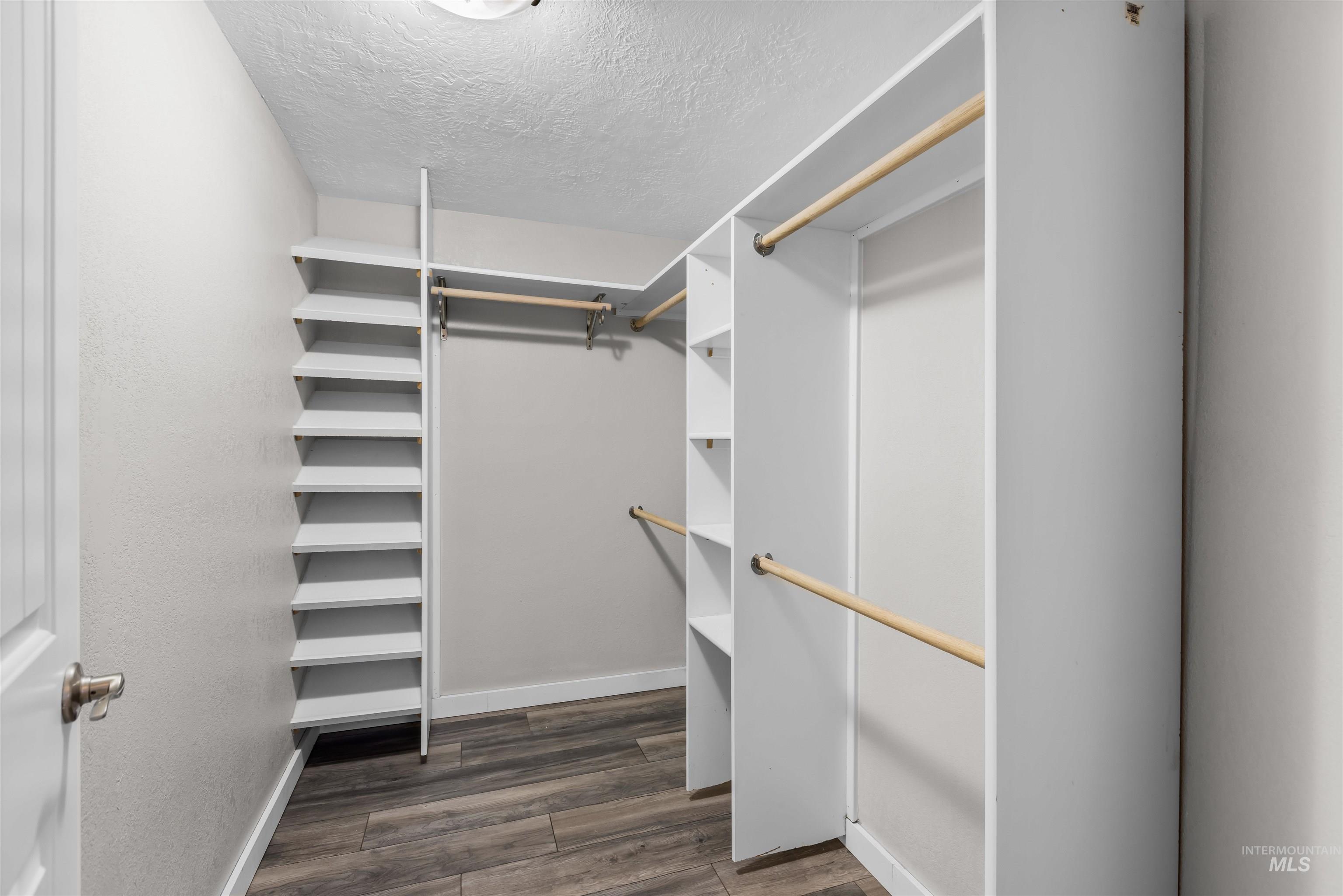 Walk-in closet with built-in shelves, wooden hanging rods, and wood-look flooring.