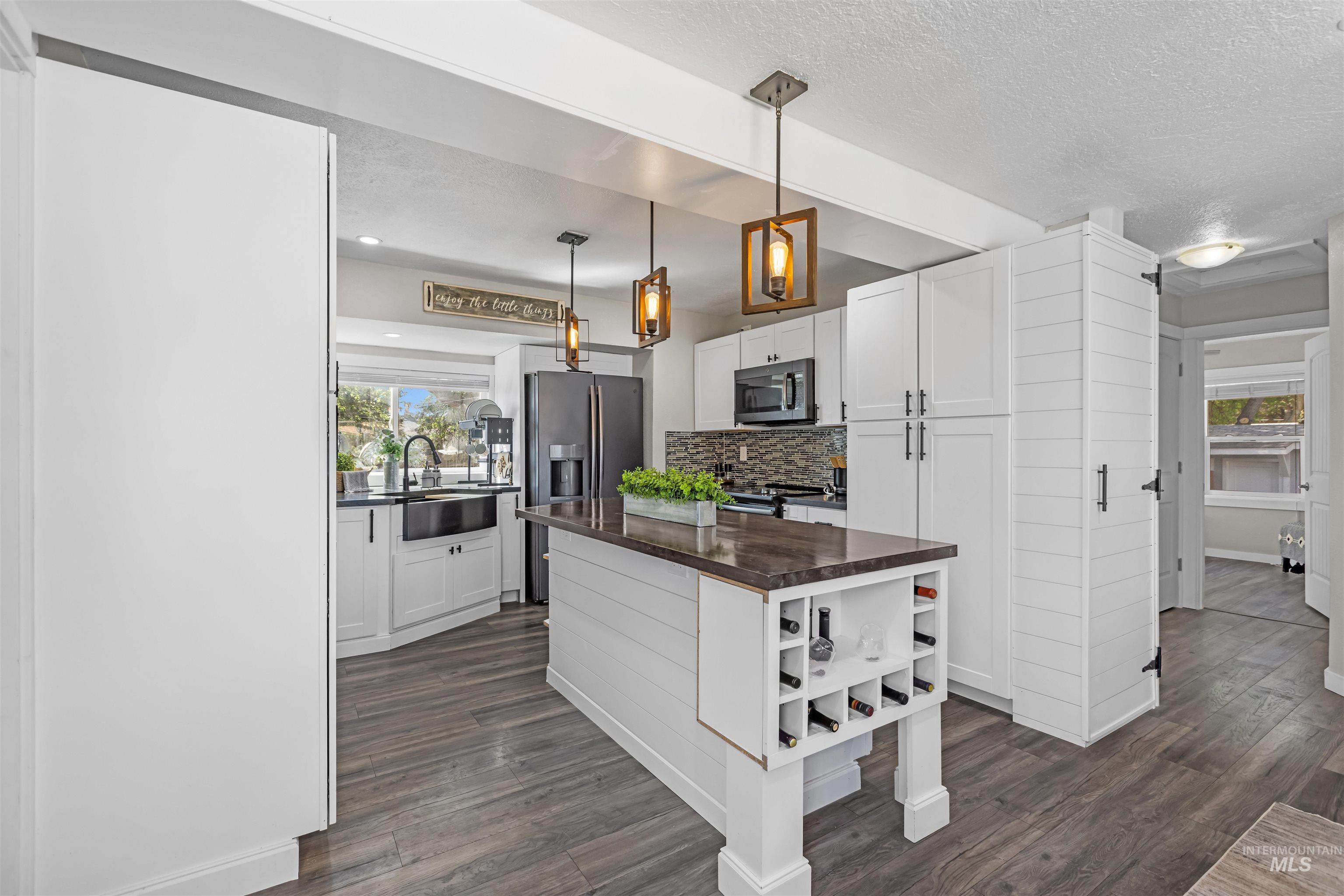 Kitchen with white shaker cabinets, a large island, dark countertop, and built-in wine storage.