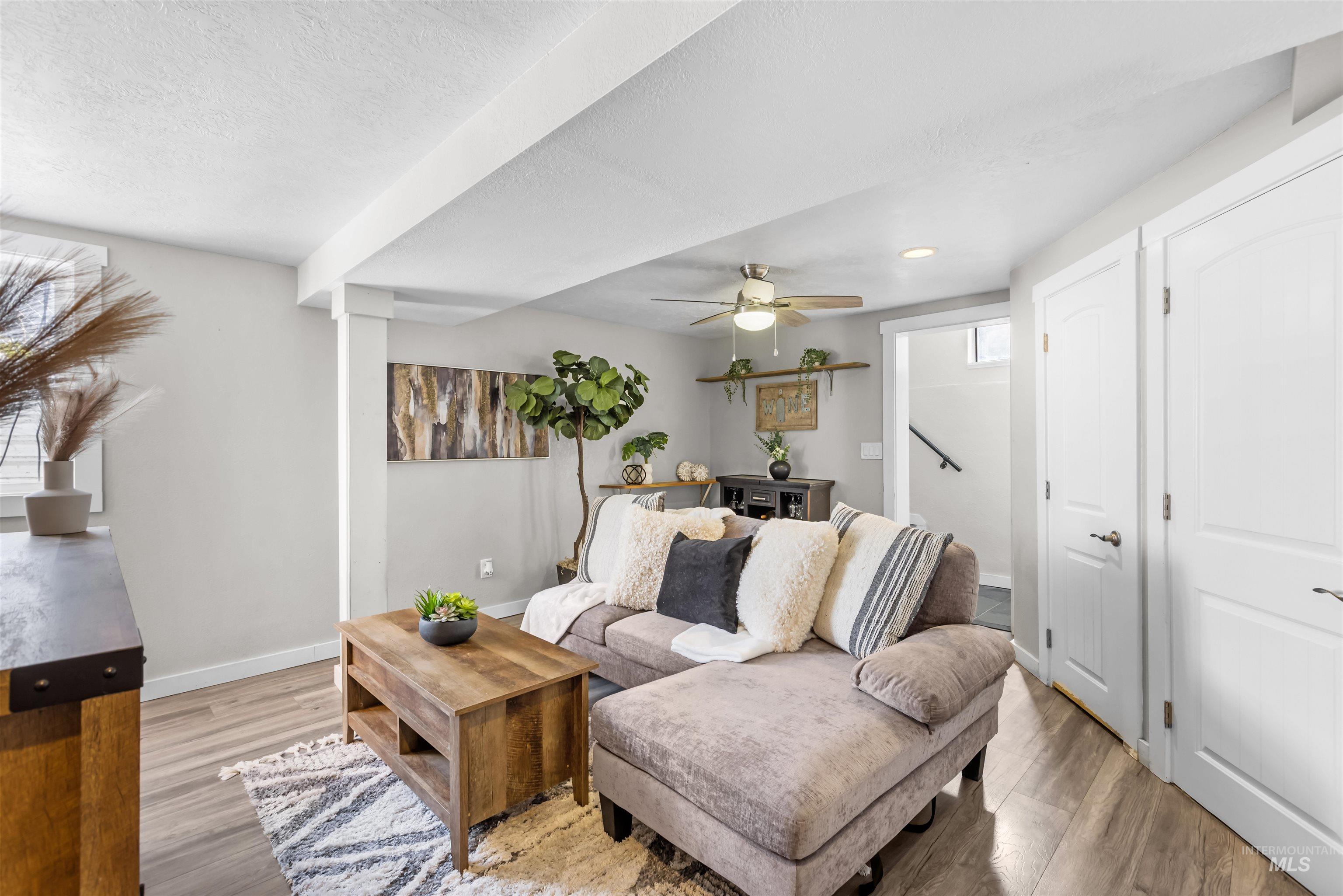 Staged living room with a gray sectional, wood coffee table, patterned rug, and ceiling fan.