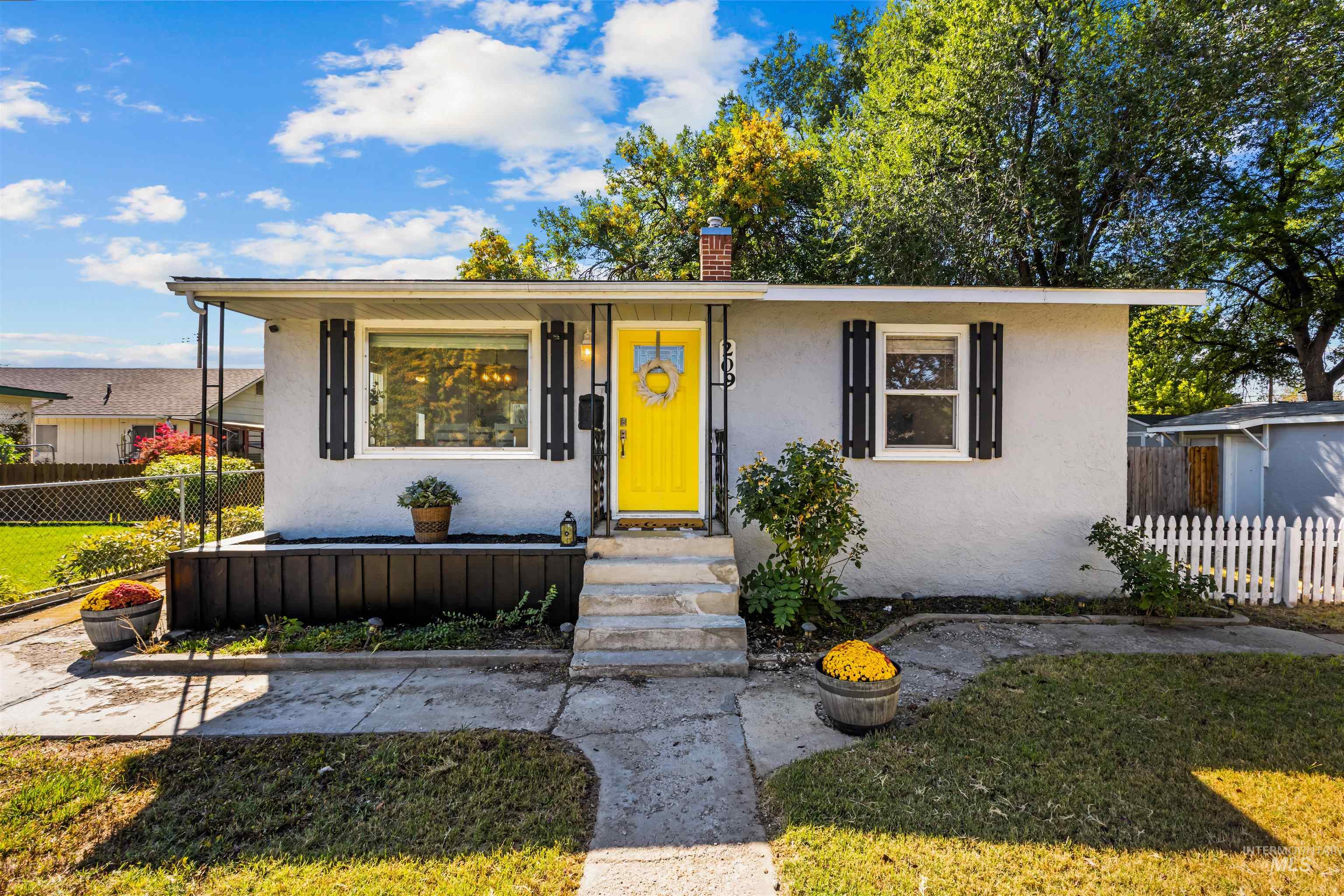 Single-story white stucco house with a bright yellow front door, black shutters, and a small raised porch.