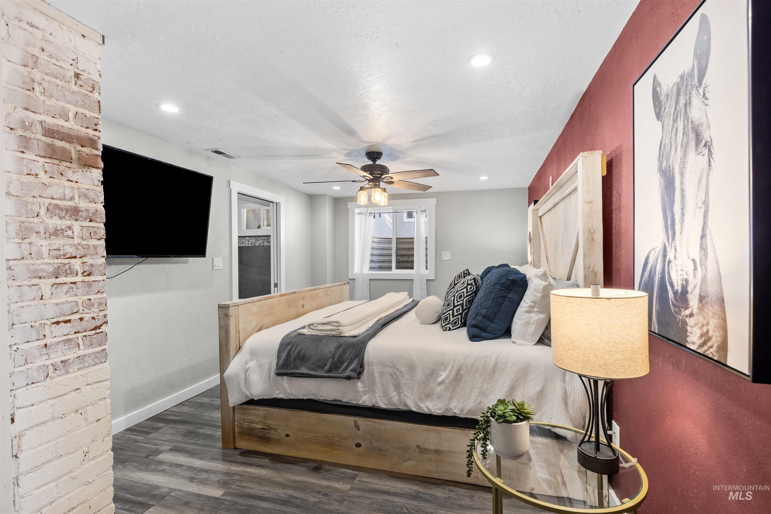Staged bedroom with a wooden bed, burgundy accent wall, large horse artwork, and exposed white brick.