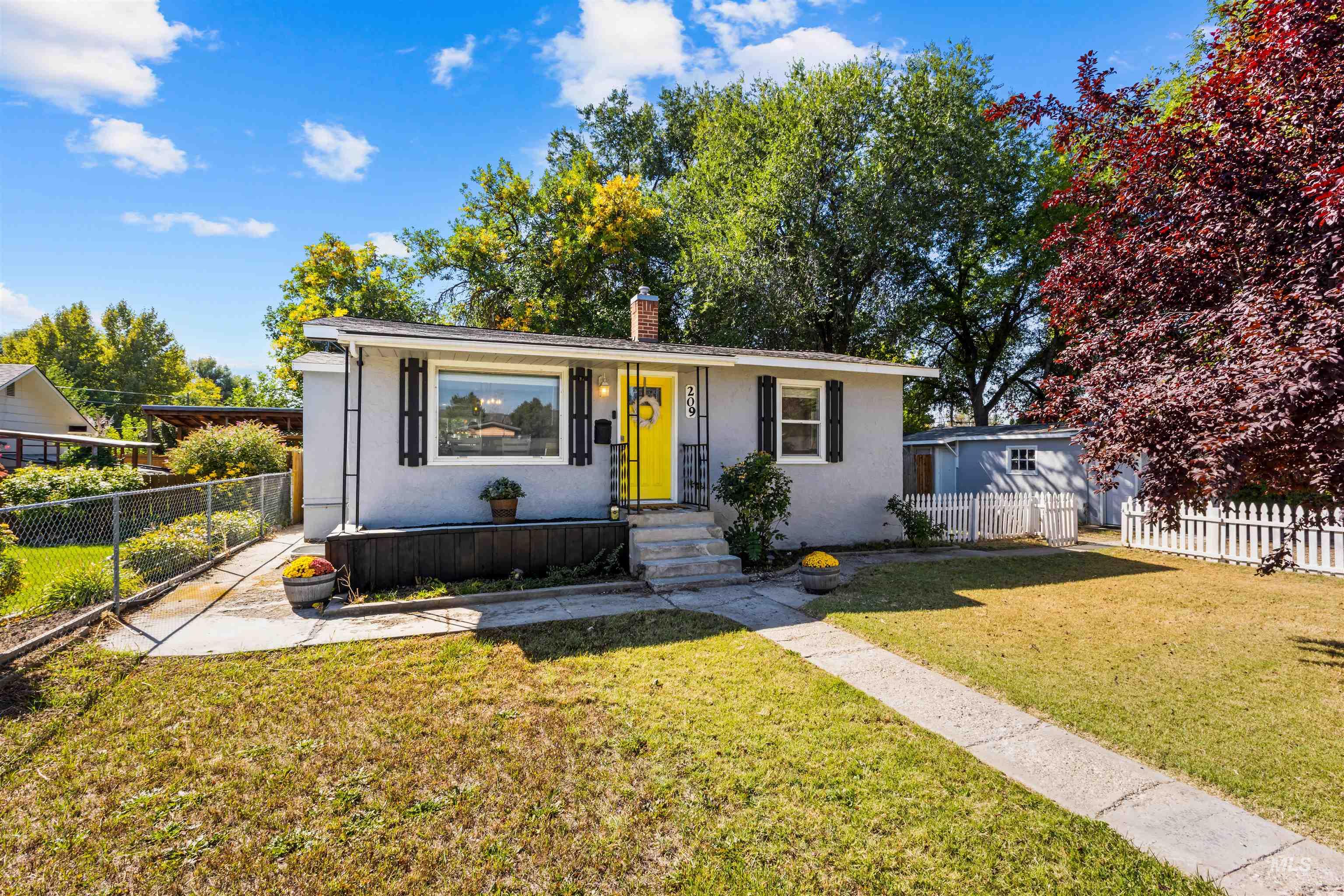 Single-story white house with black shutters, a bright yellow front door, and a concrete walkway.