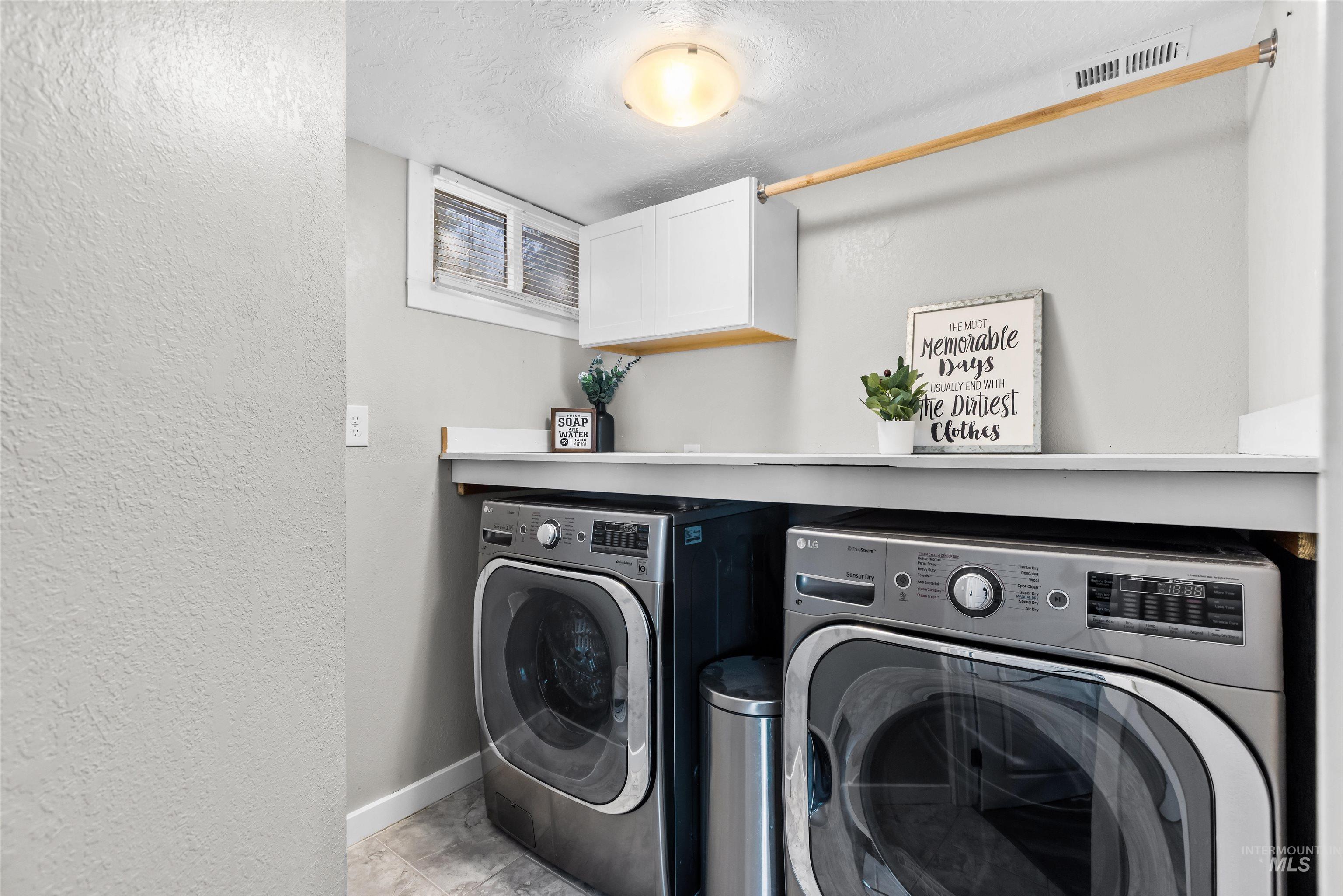 Laundry room with front-loading washer and dryer beneath a counter, with a window and overhead cabinet.