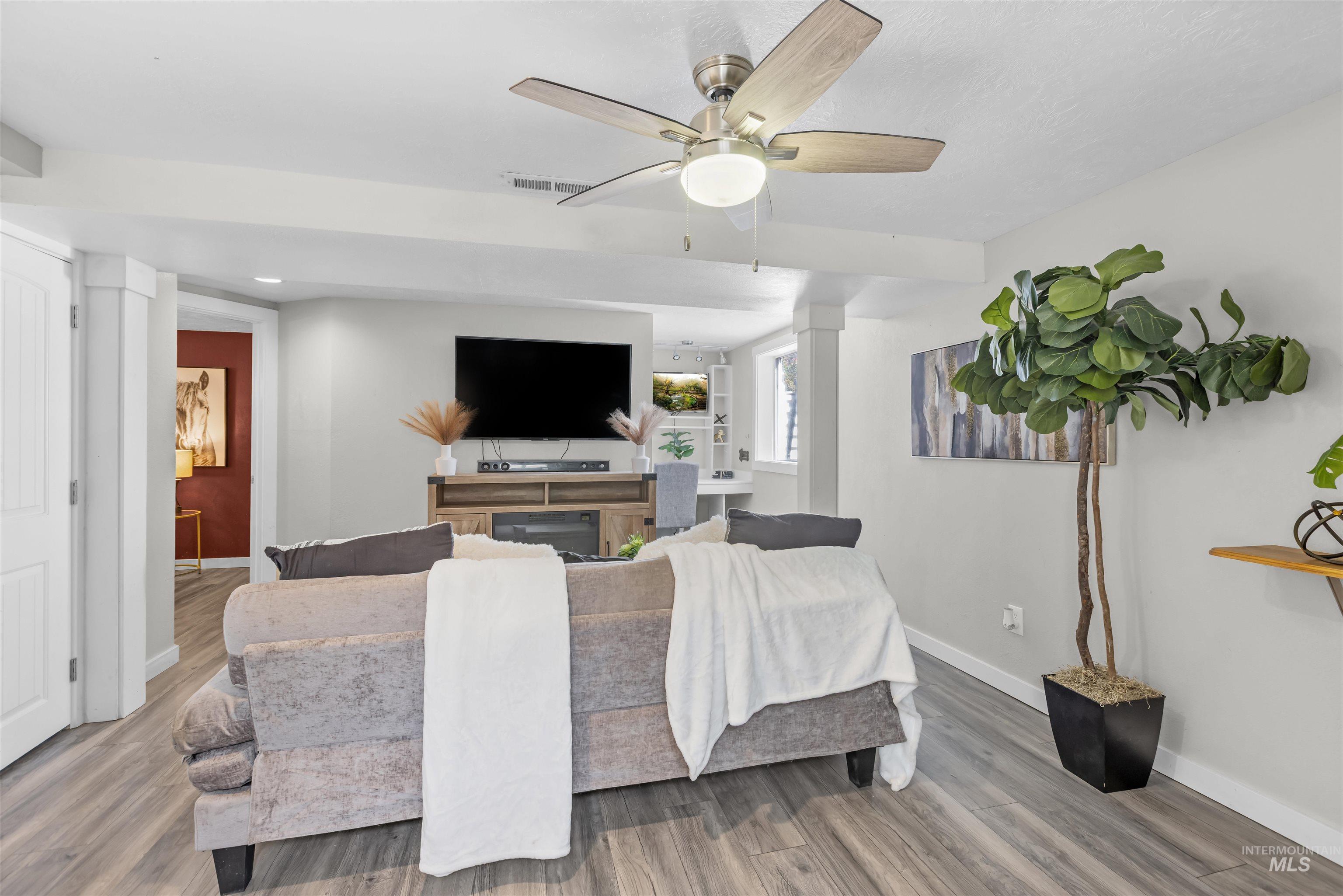Staged living room with a gray sofa, ceiling fan, television, and tall potted plant.