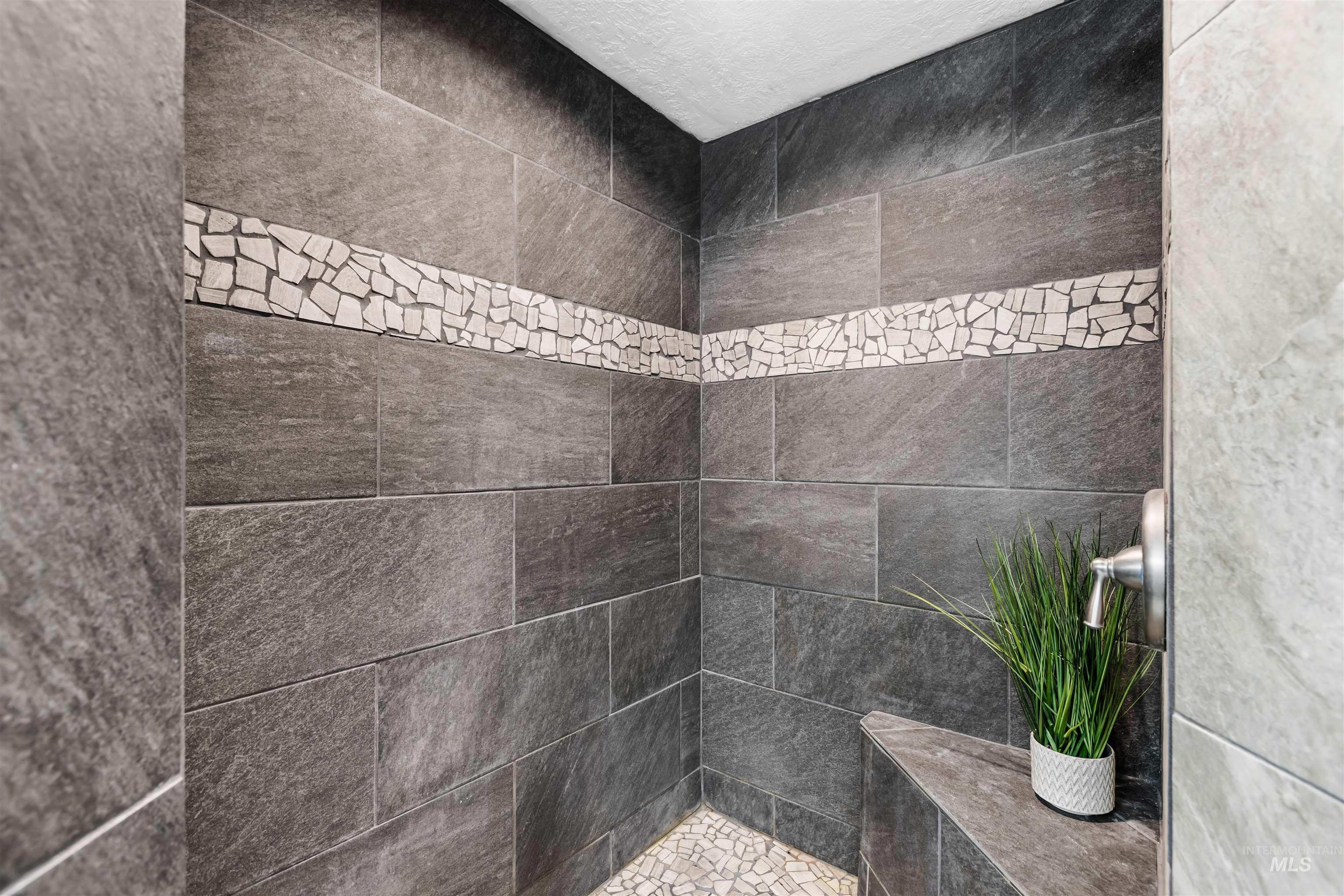 Walk-in shower with charcoal-gray tile, a pale mosaic accent band, built-in bench, and potted plant.