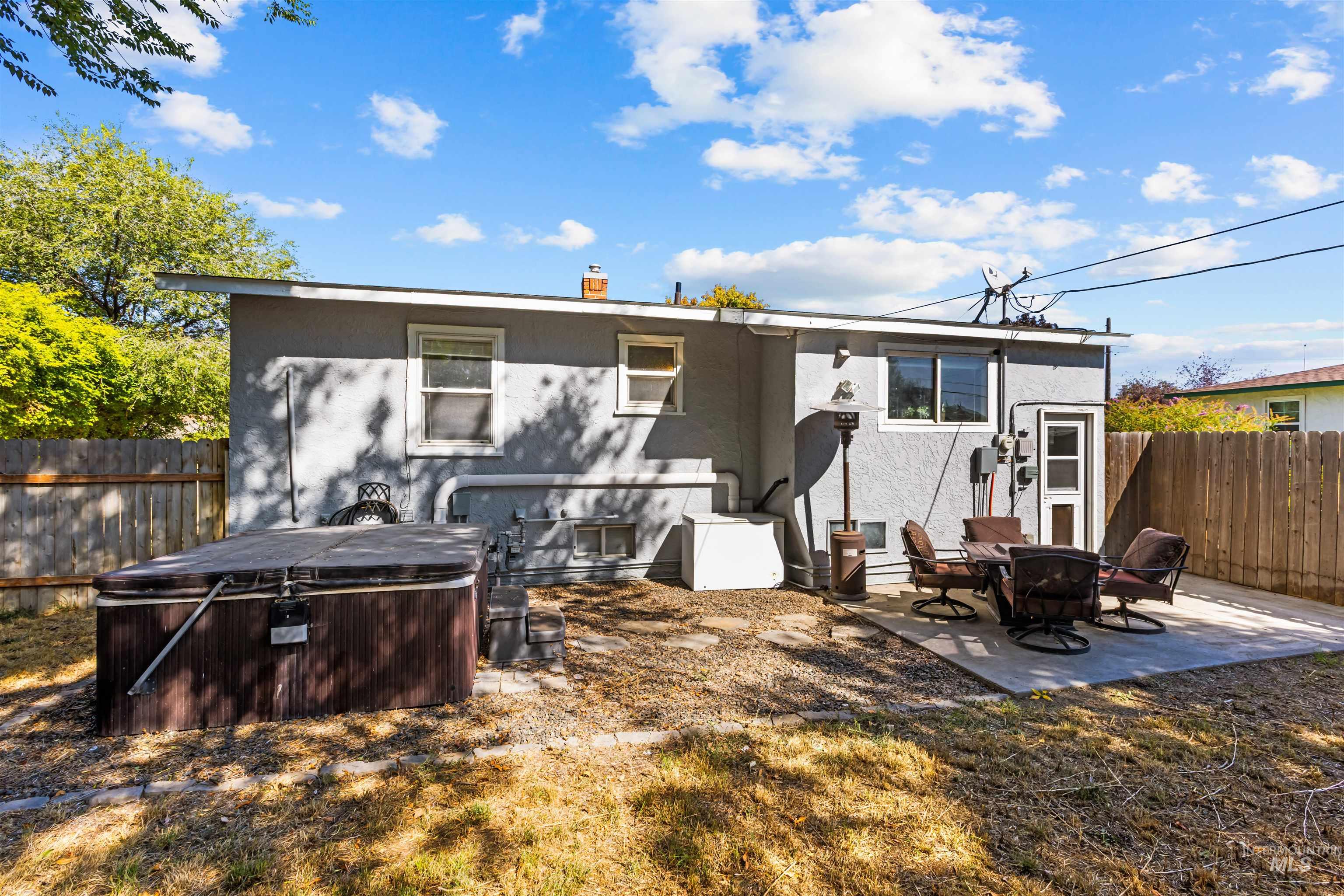 Home’s fenced backyard with a covered hot tub and a furnished concrete patio.
