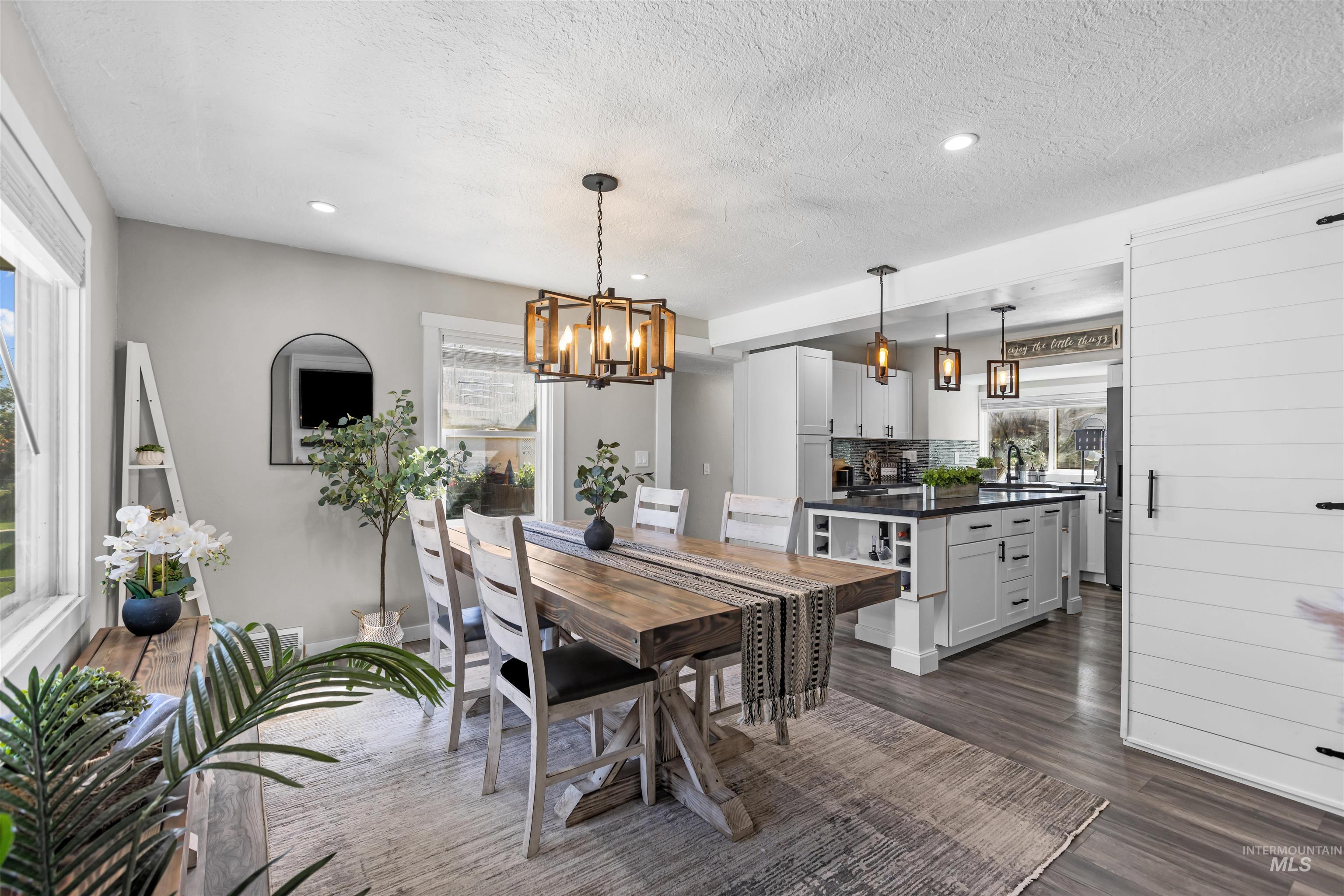 Dining area with a rustic wood table, white chairs, and an adjoining white kitchen.