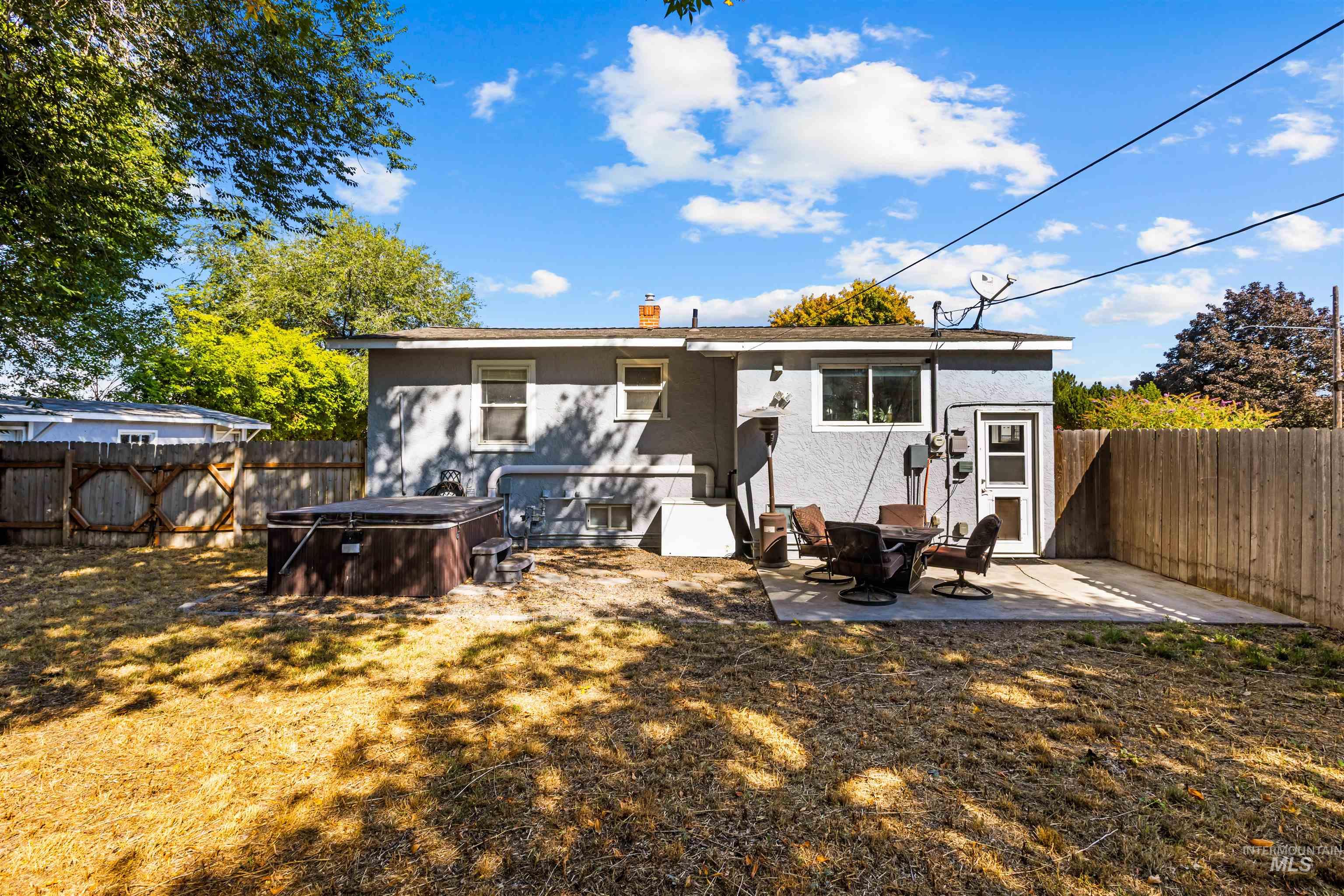 Rear of a gray house with a fenced yard, hot tub, and patio seating.