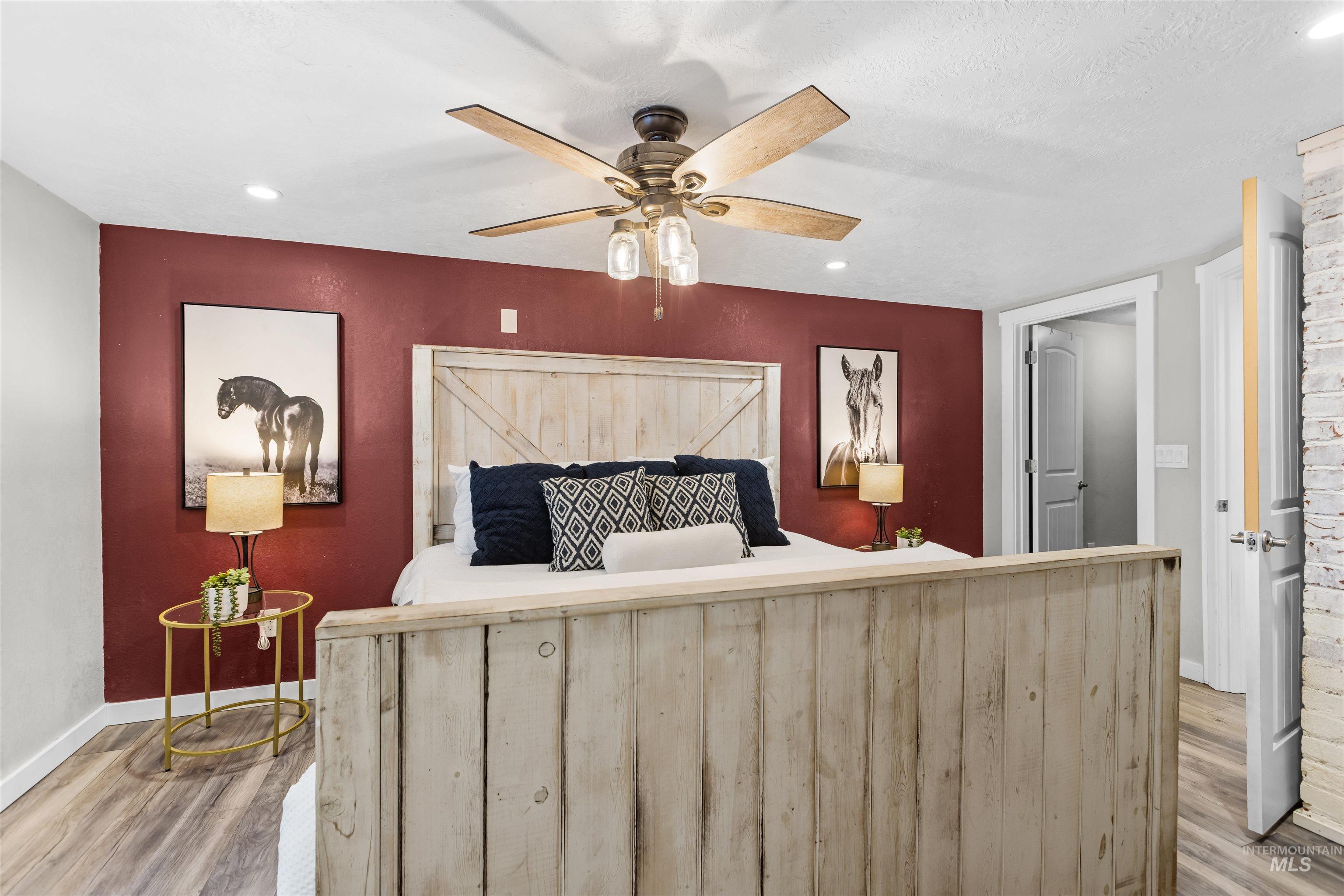 Furnished bedroom with a burgundy accent wall, rustic wood bed, and horse portraits.