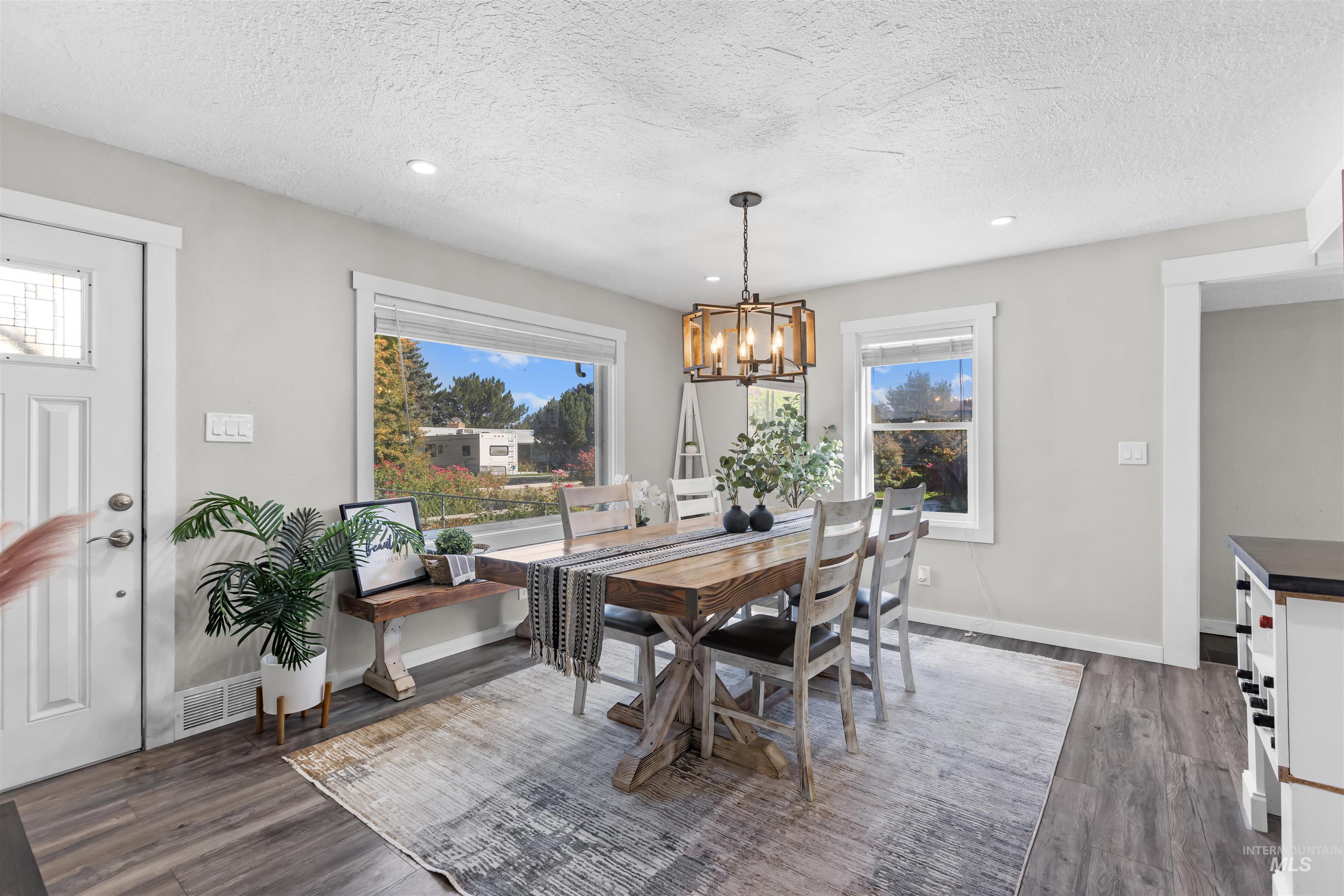 Dining room with a rustic wood table, large windows, and a geometric pendant light.