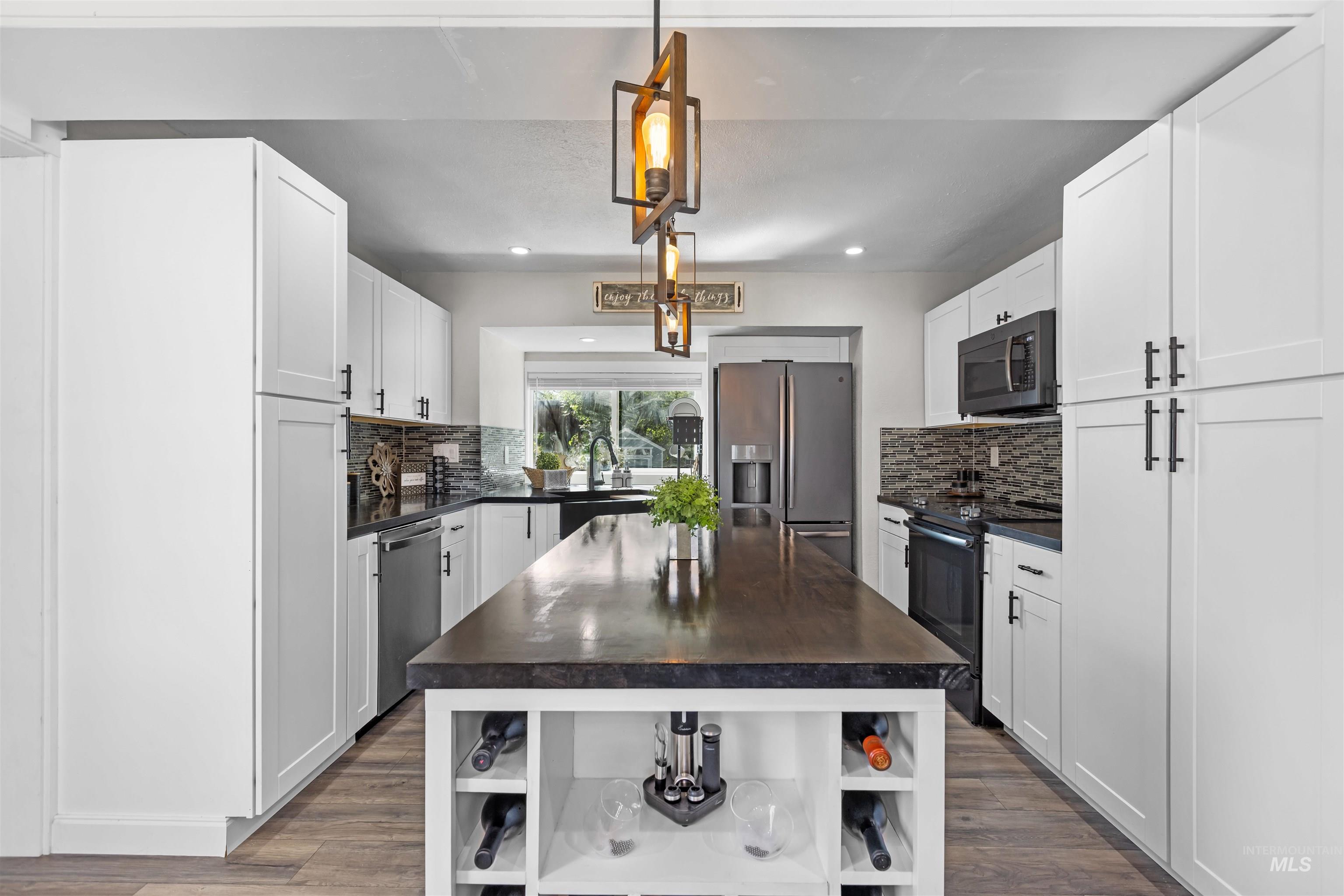 Kitchen with white cabinets, stainless steel appliances, and a large dark-topped island with wine storage.