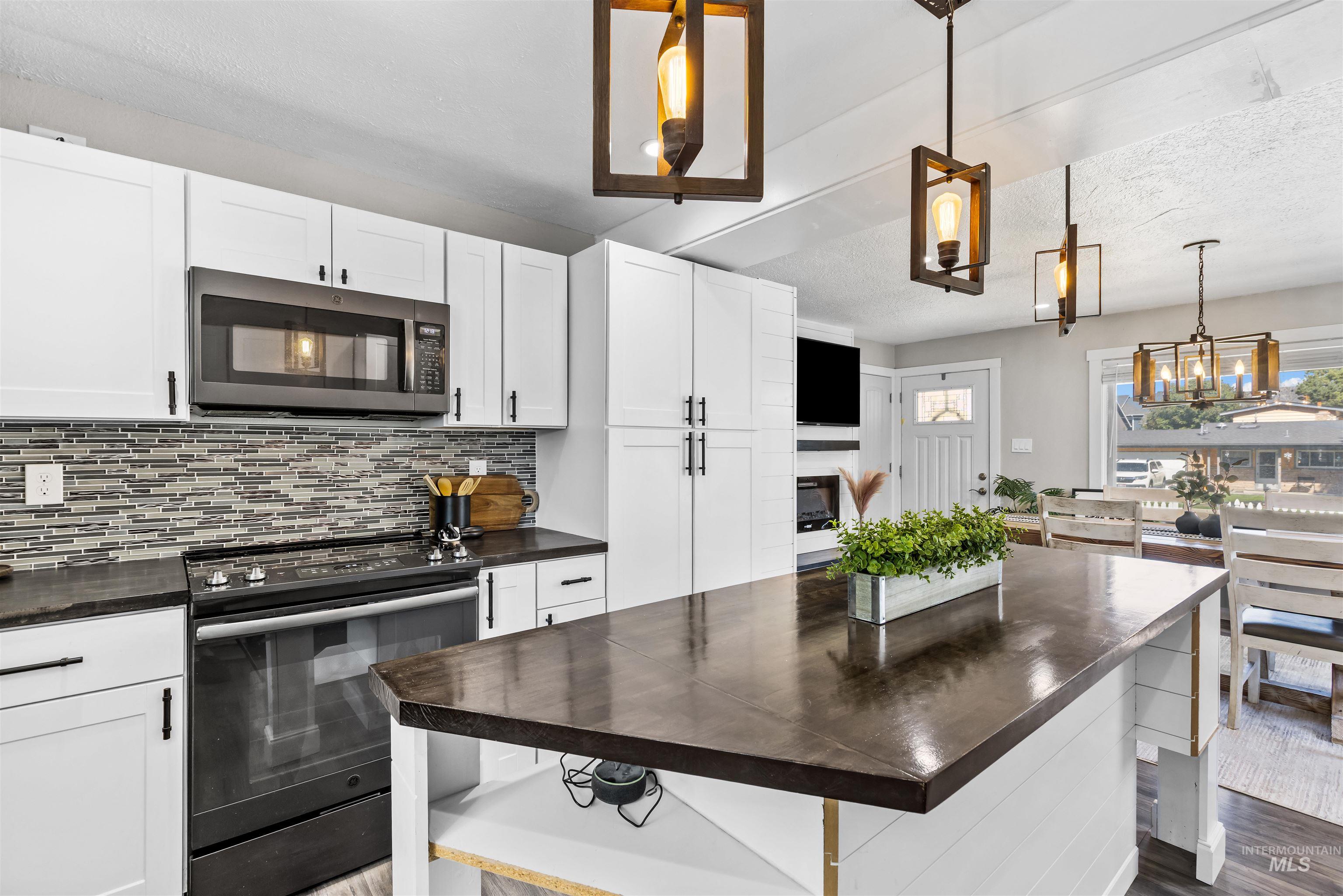Kitchen with white cabinets, a dark wood island, and a long tile backsplash.
