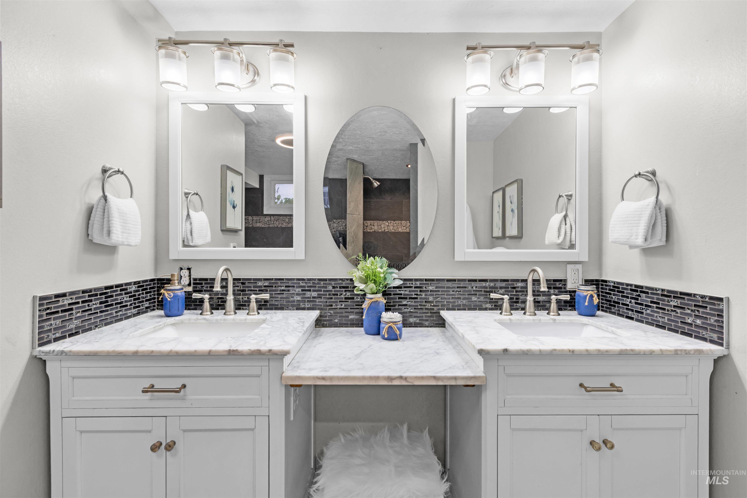 Bathroom double vanity with marble-look counters, dark tile backsplash, and three mirrors.