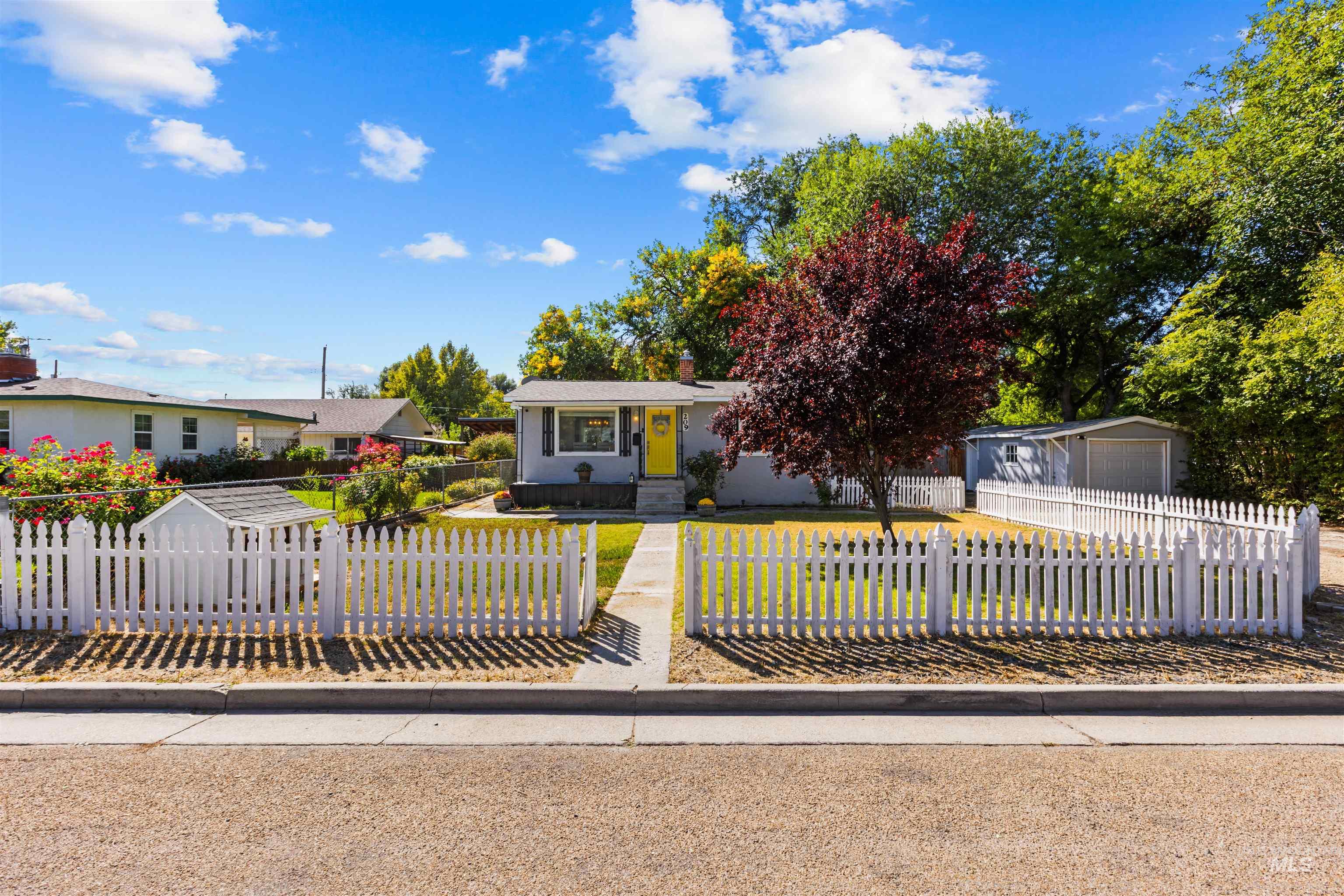 Single-story home with a yellow front door, white picket fence, and detached garage.