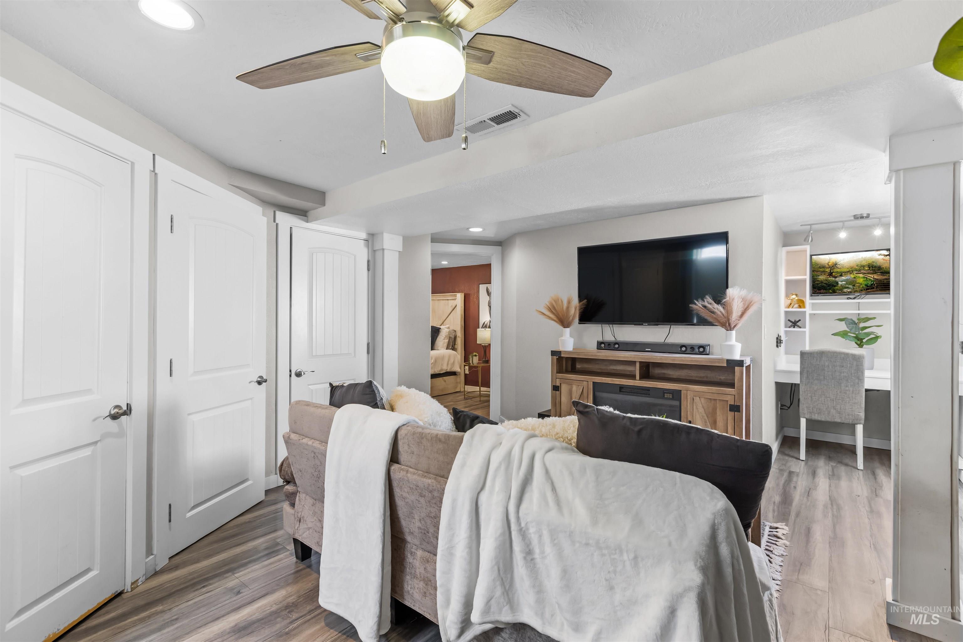 Staged living room with a ceiling fan, television, wood media console, and built-in desk nook.