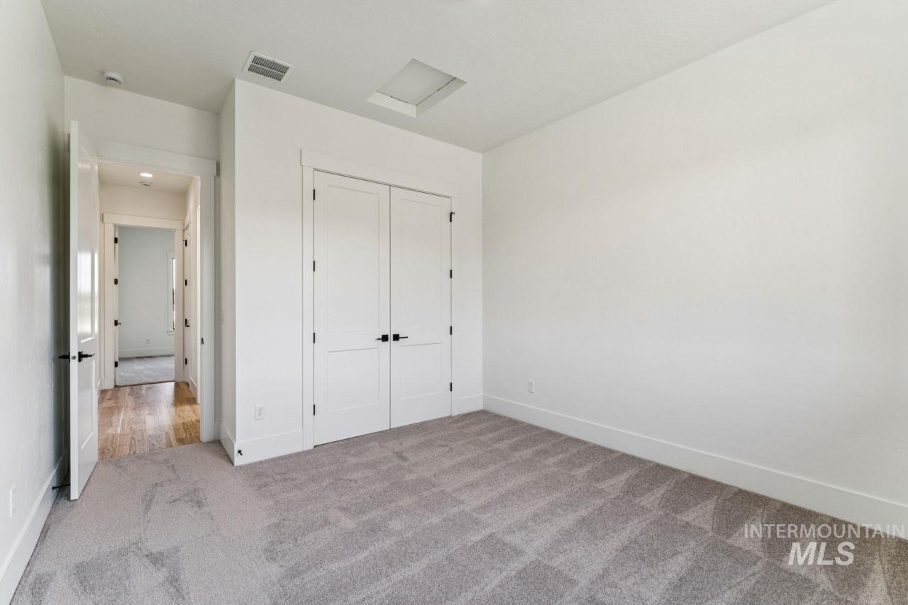 Unfurnished bedroom with gray carpet, double closet doors, and a hallway beyond.