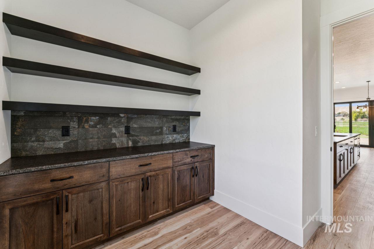 Built-in wooden cabinets with dark stone backsplash and floating shelves beside a doorway to the kitchen.