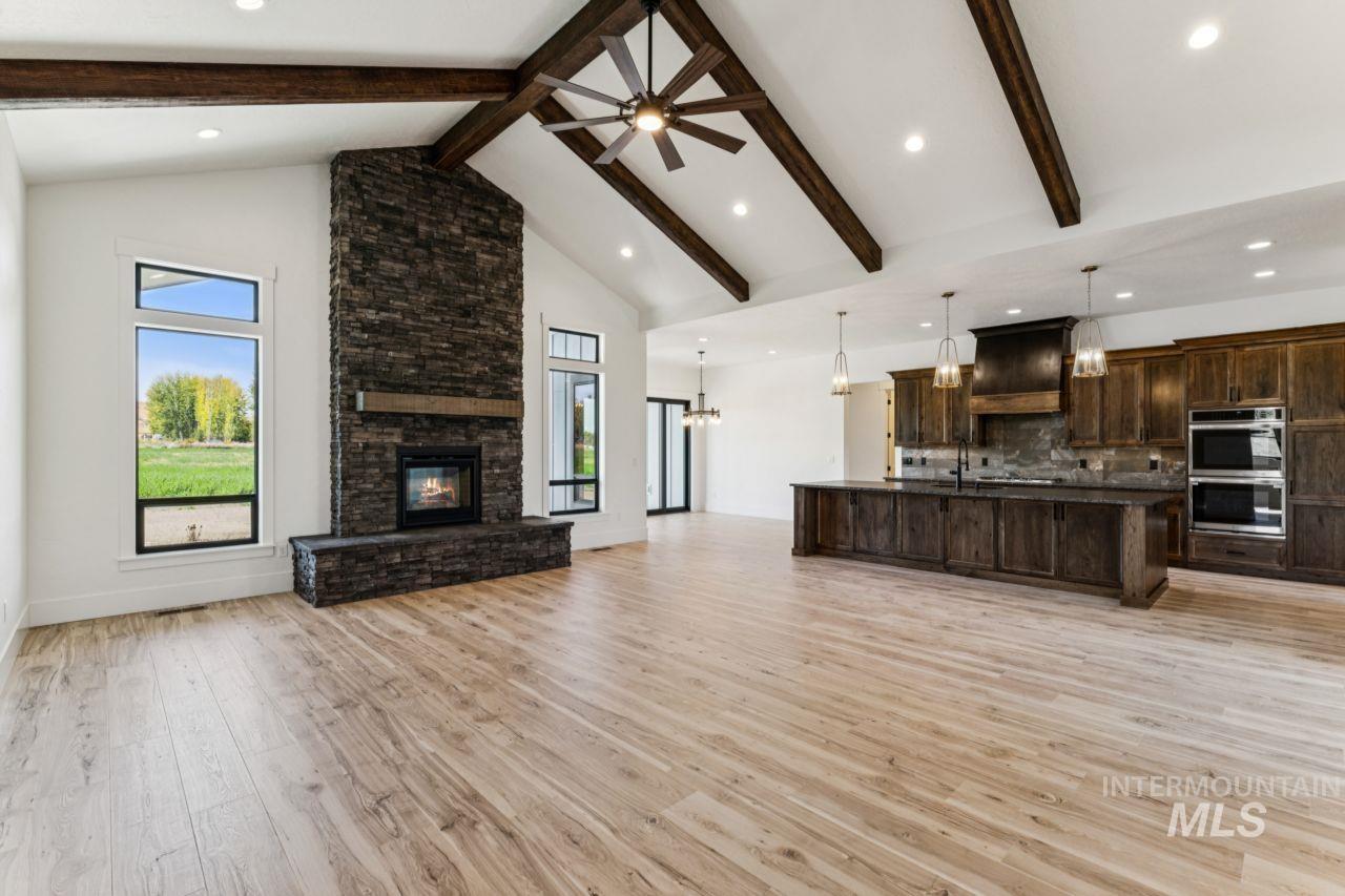 Open living room and kitchen with a tall stone fireplace and vaulted ceiling with exposed beams.
