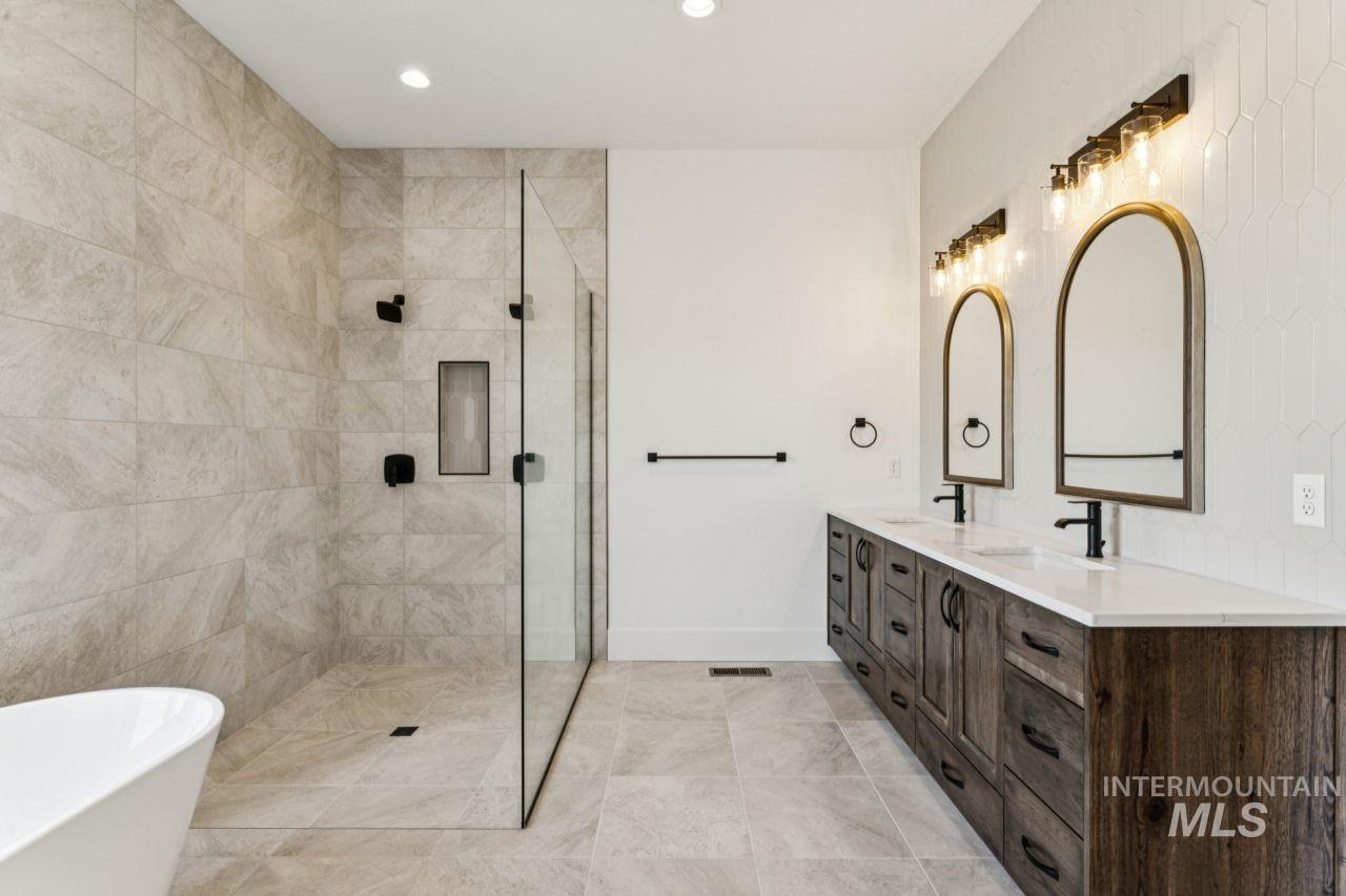 Bathroom with a tiled glass shower, double vanity, arched mirrors, and freestanding tub.