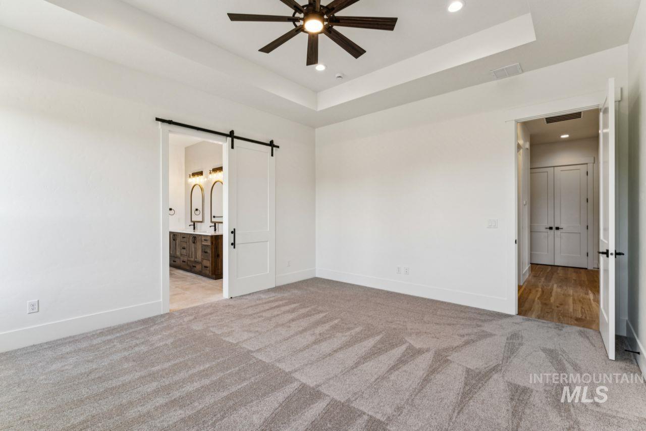 Empty carpeted bedroom with a dark ceiling fan and an open barn door to the bathroom.