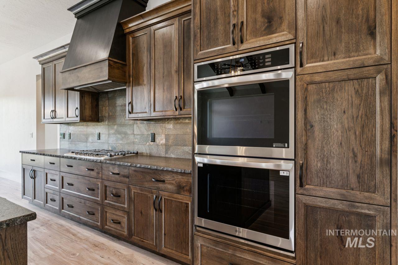 Kitchen with dark wood cabinets, double wall ovens, and a gas cooktop beneath a large range hood.