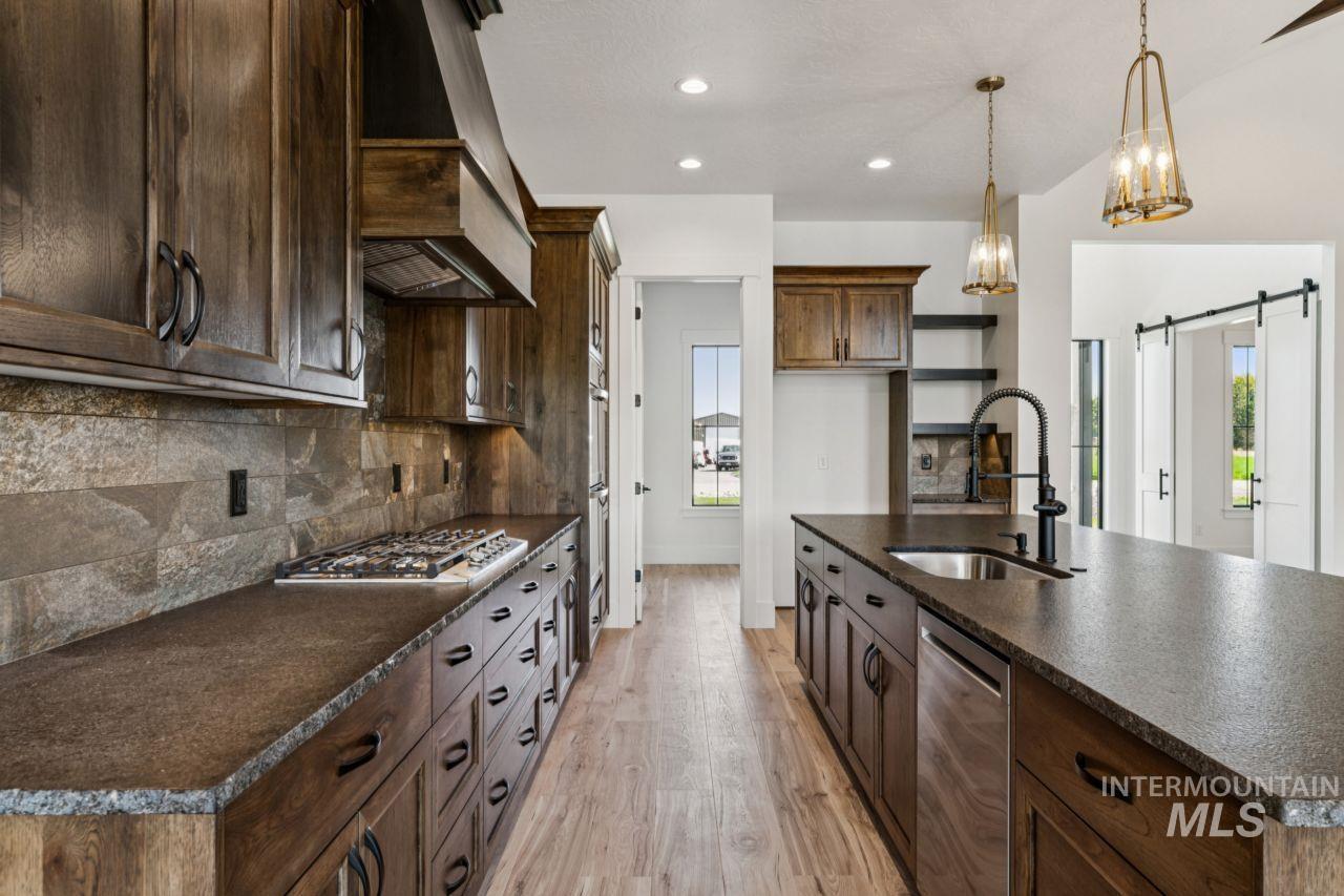 Kitchen with dark wood cabinets, stone counters, gas cooktop, and a large island with pendant lights.