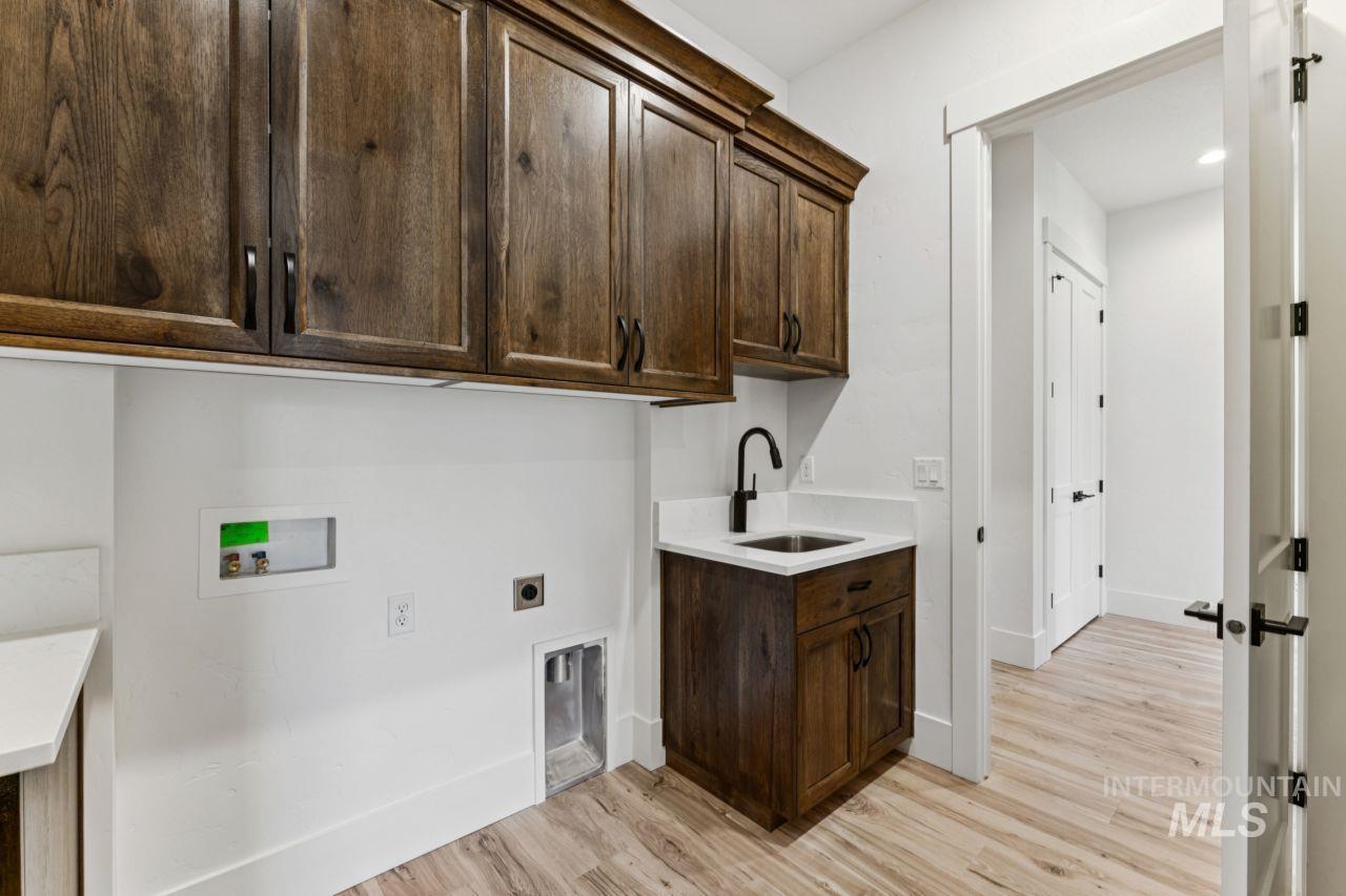 Laundry room with dark wood cabinetry, a utility sink, washer and dryer hookups, and light wood-look flooring.