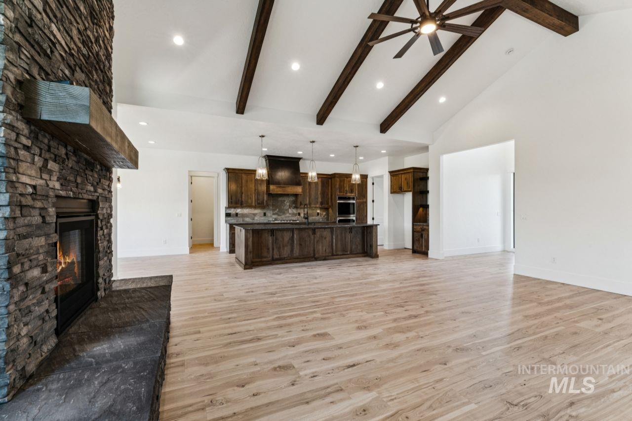 Open kitchen and living area with dark wood cabinetry, stone fireplace, and exposed ceiling beams.