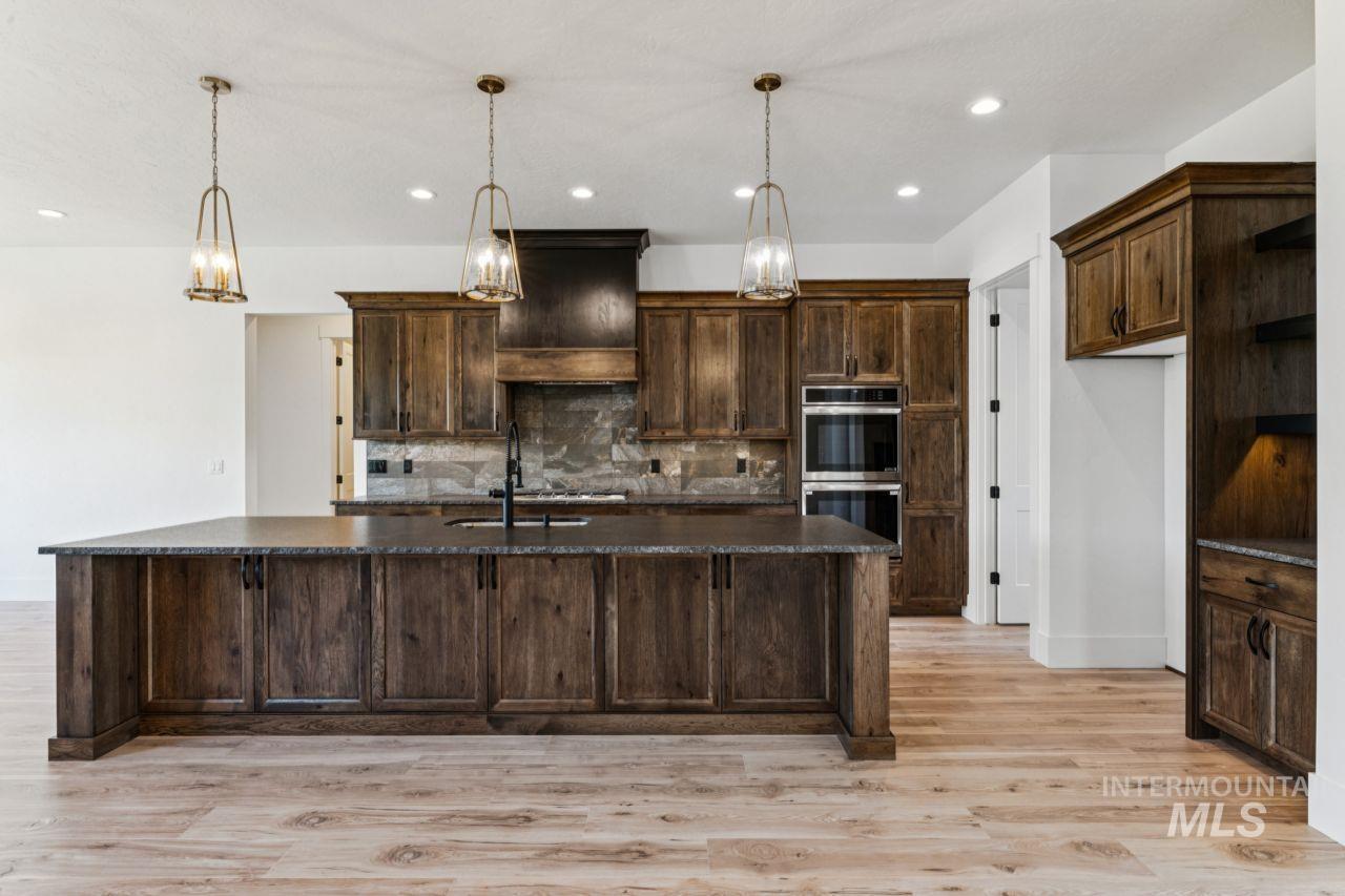 Kitchen with dark wood cabinetry, a large island, stone backsplash, and pendant lights.