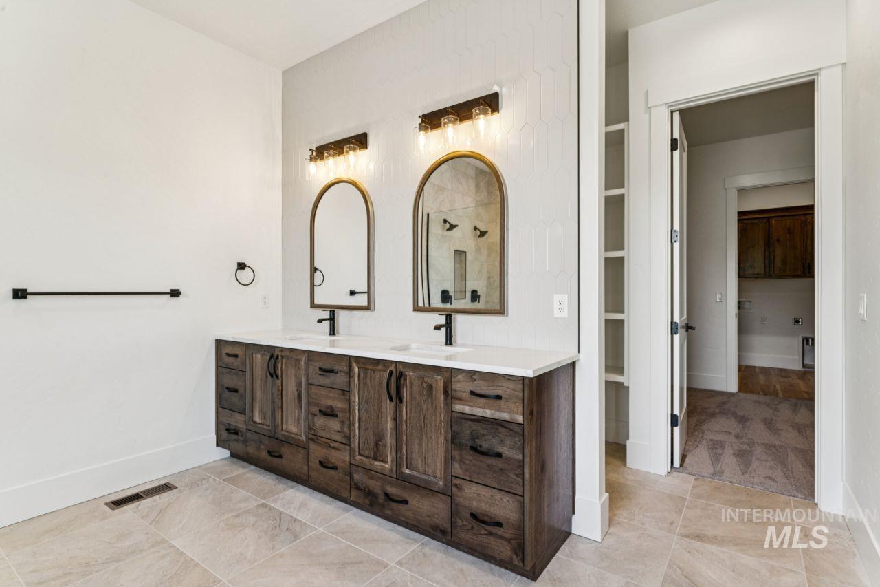 Bathroom with a dark wood double vanity, two arched mirrors, and pale tile floors.