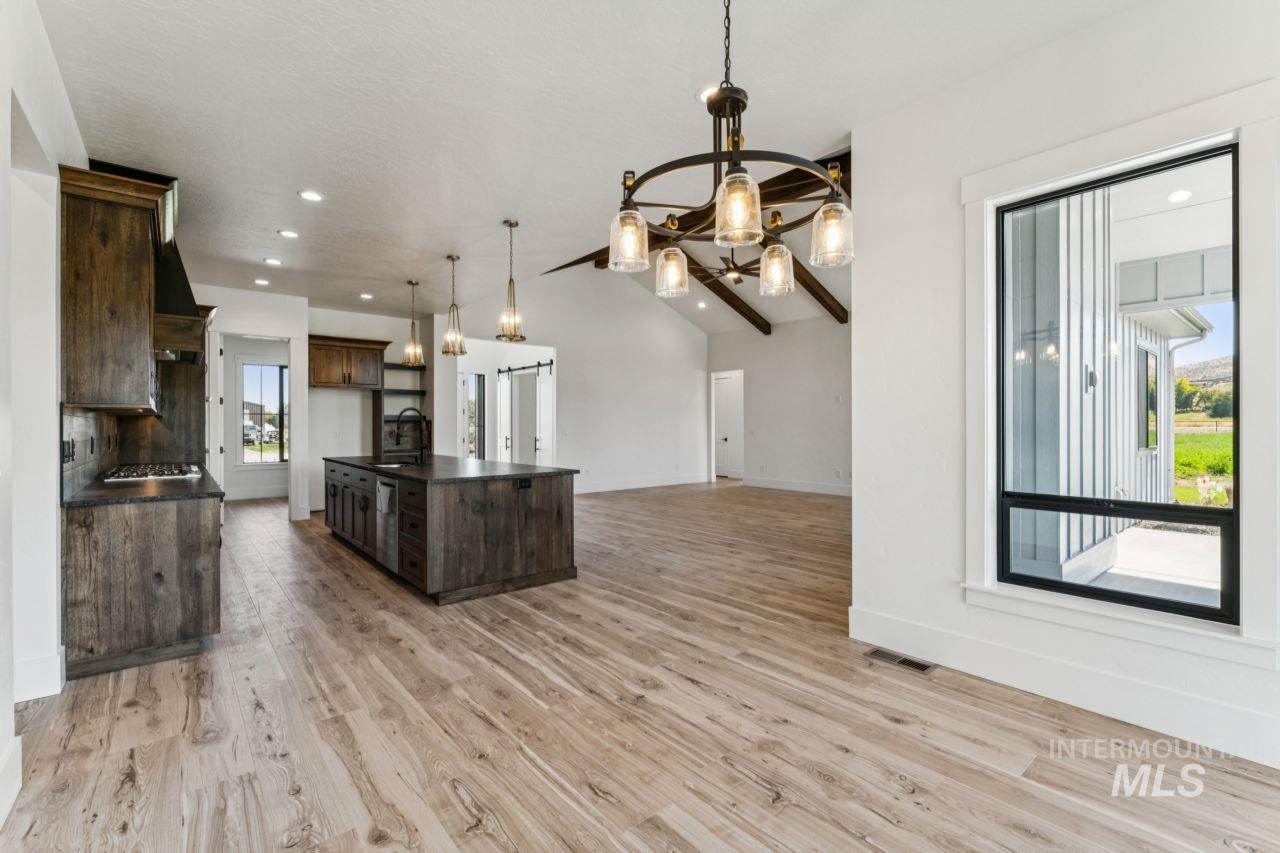 Open kitchen and living area with a large dark island, wood-look floors, vaulted ceiling, and exposed beams.