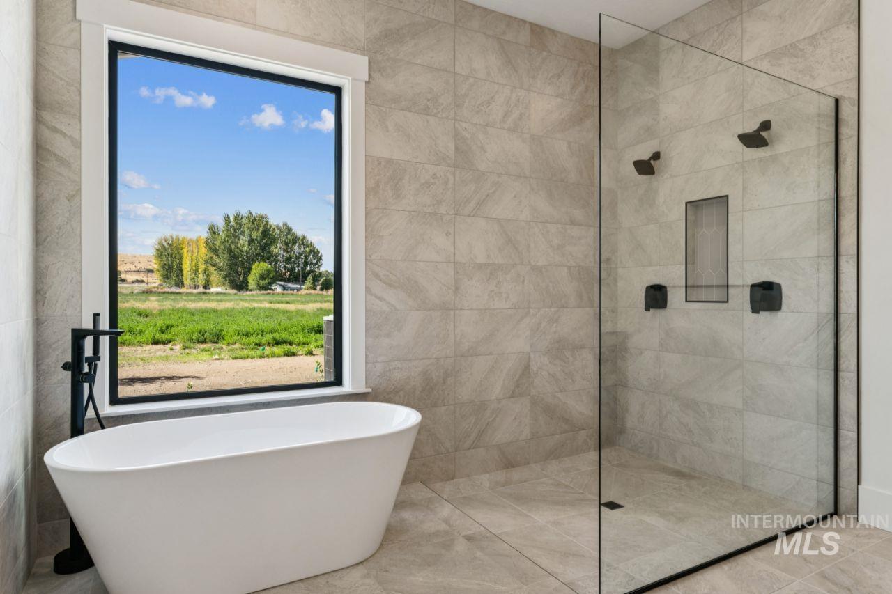 Bathroom with a freestanding tub, glass shower, and a window overlooking green fields.
