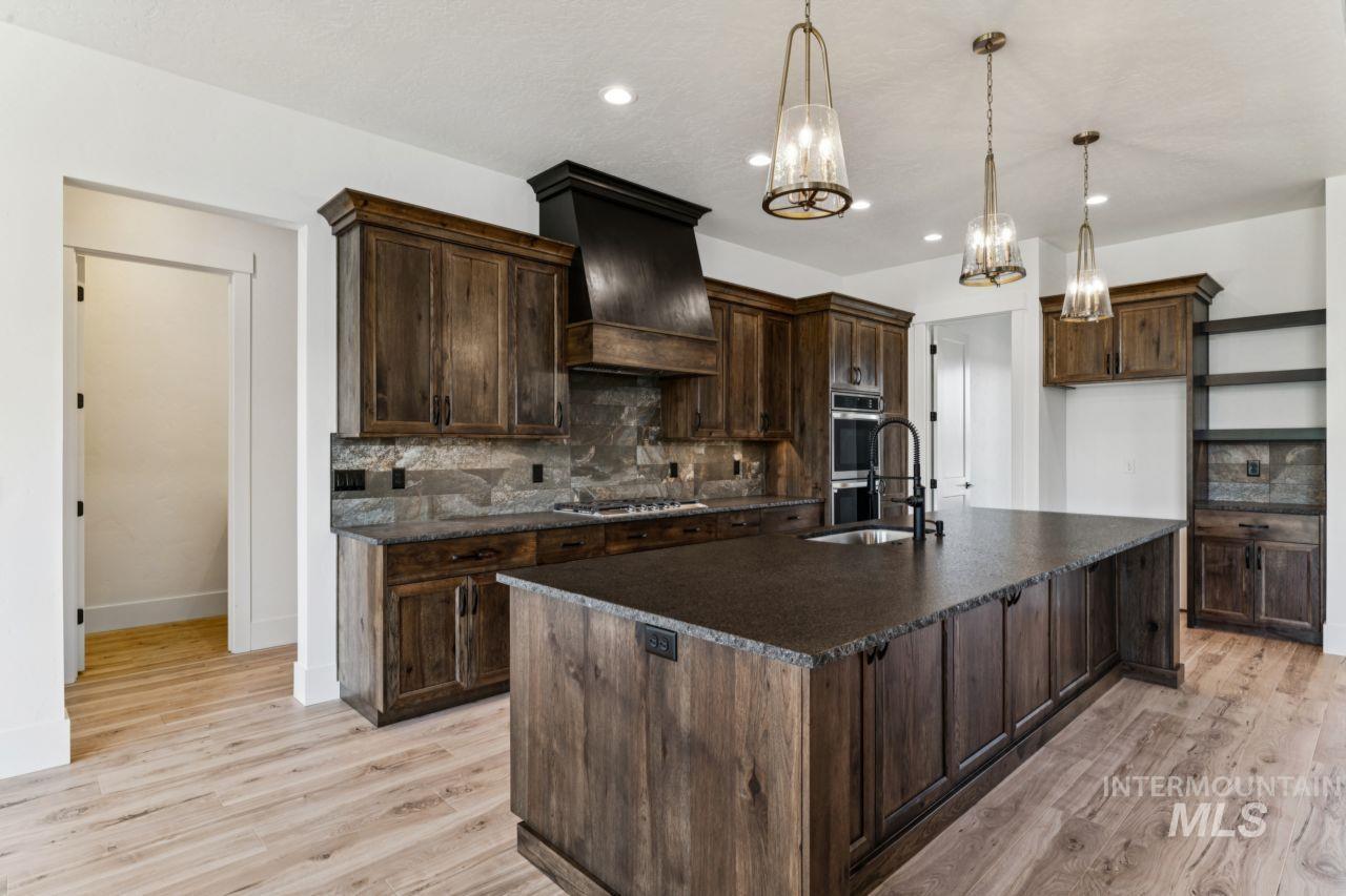 Kitchen with dark wood cabinetry, a large stone island, and three pendant lights.