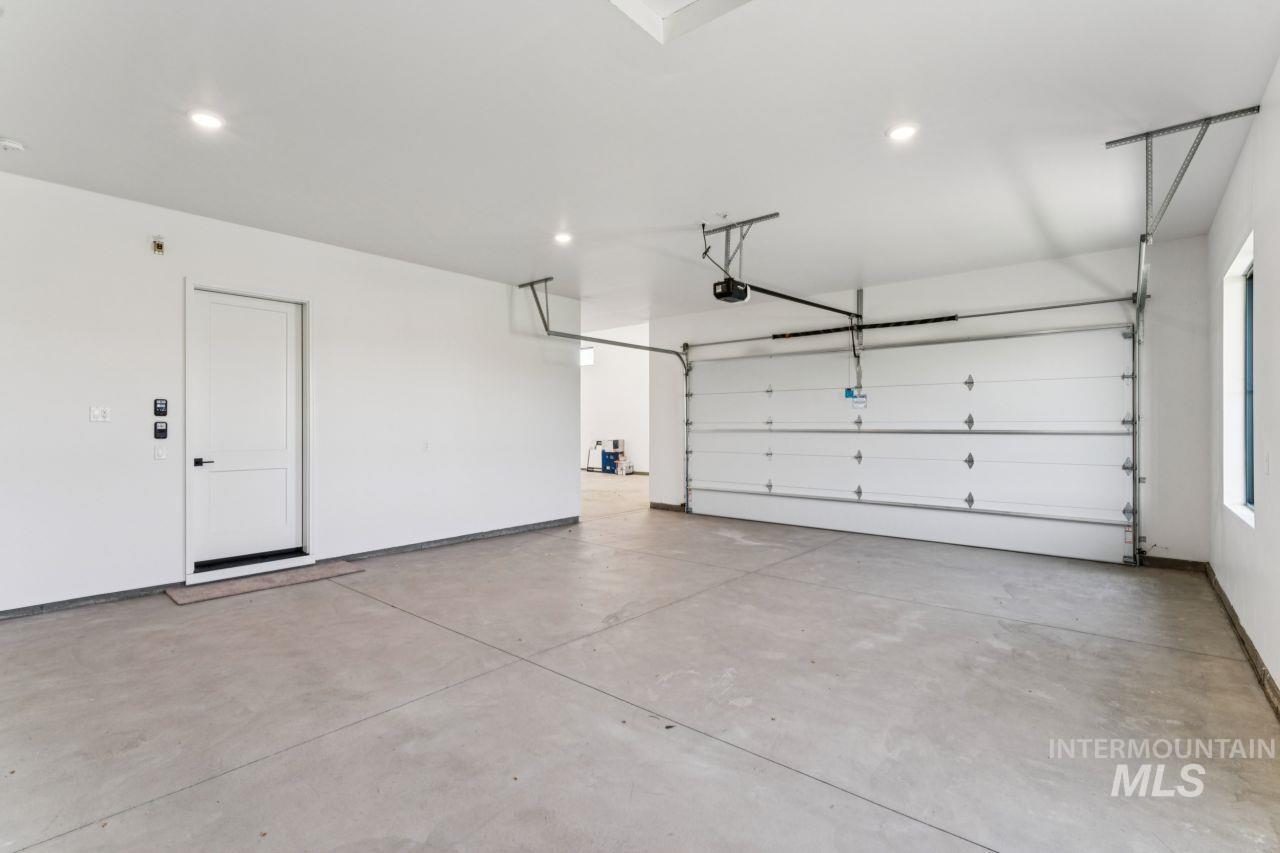 Empty garage with a wide concrete floor, sectional overhead door, and separate interior access door.