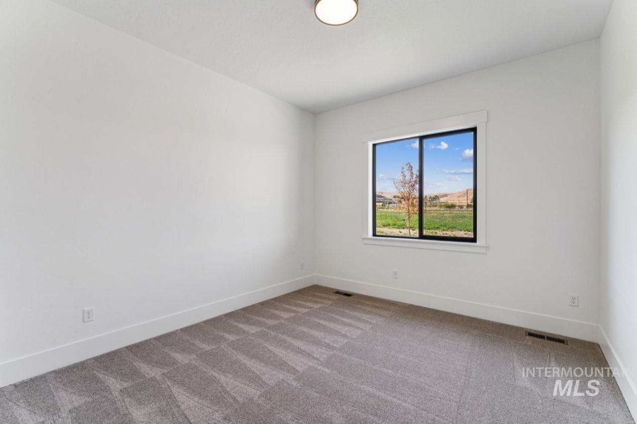 Empty bedroom with gray patterned carpet and a window overlooking green fields and low hills.