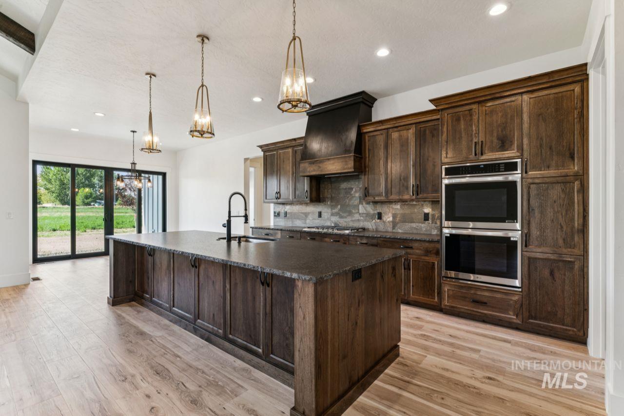 Kitchen with dark wood cabinetry, a large island, stainless steel double ovens, and sliding glass doors.