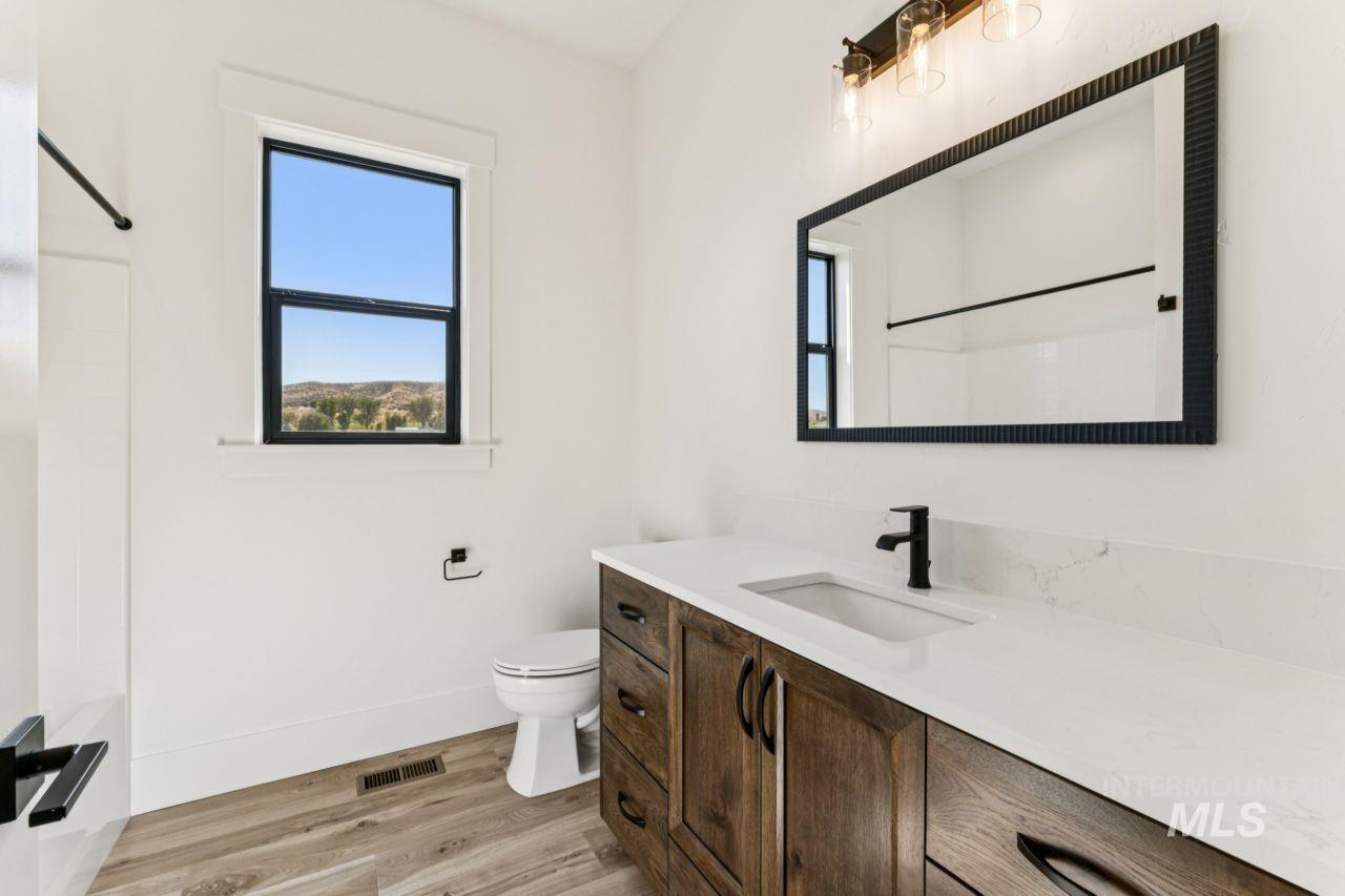 Modern bathroom with a wood vanity, black-framed mirror, and a window overlooking trees and hills.