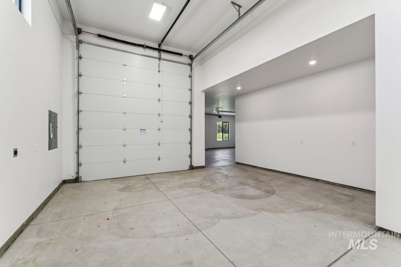 Empty garage with a large overhead door, concrete floor, and wide opening into the house.