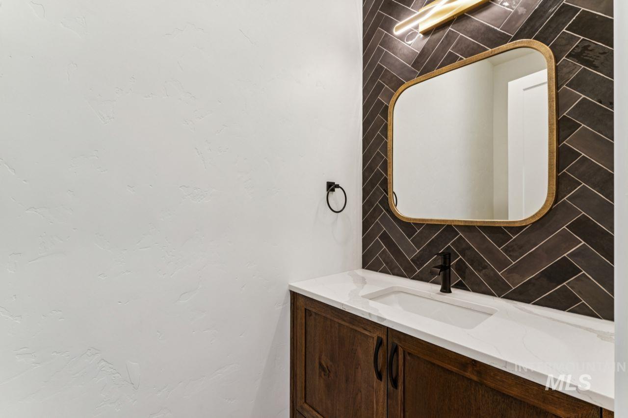 Bathroom vanity with a dark wood cabinet, white sink, herringbone tile backsplash, and gold-framed mirror.