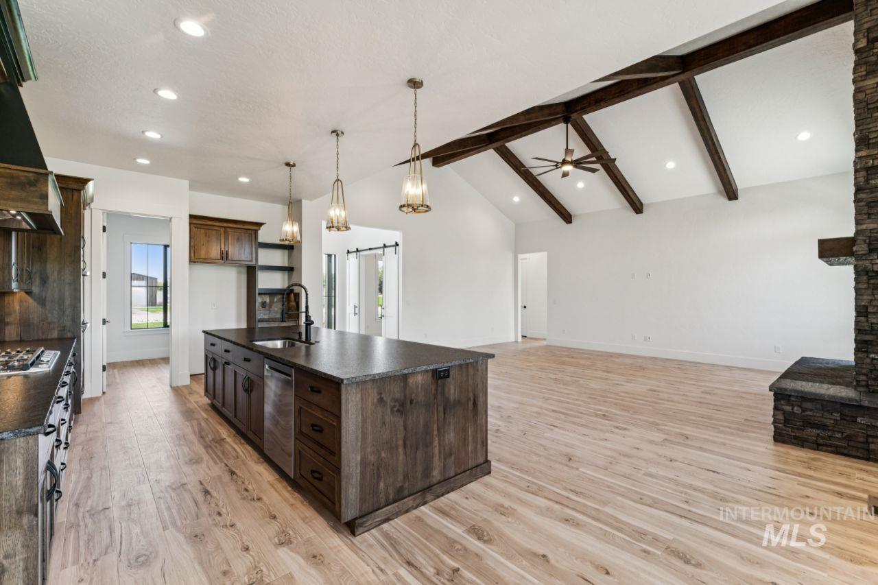 Open-plan kitchen with a dark-wood island, exposed beams, light wood floors, and stone fireplace.
