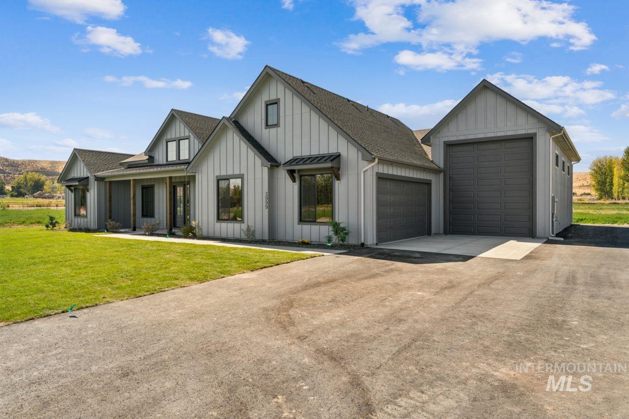 Gray farmhouse-style home with two garage doors, a broad driveway, and a green front lawn.