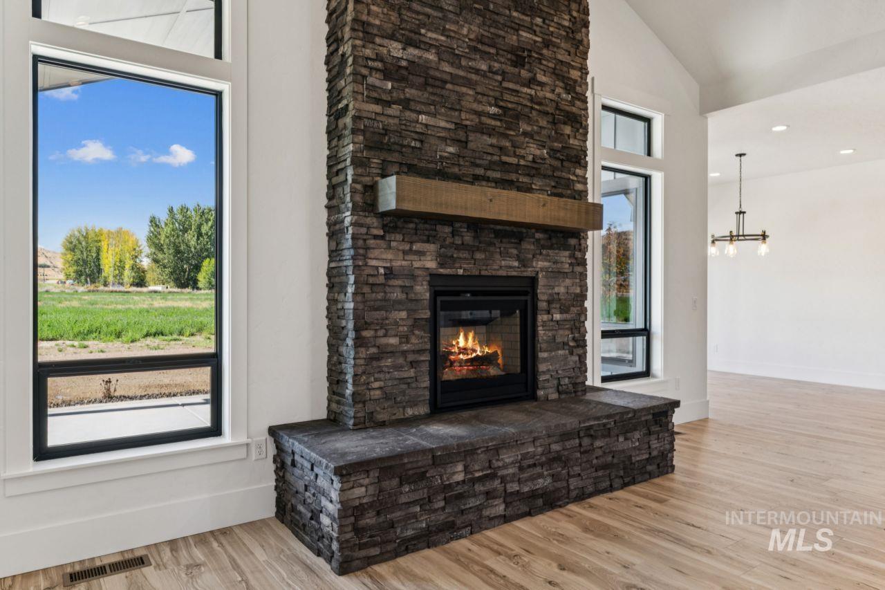 Living room with a tall stone fireplace, wood mantel, and large windows overlooking a field.