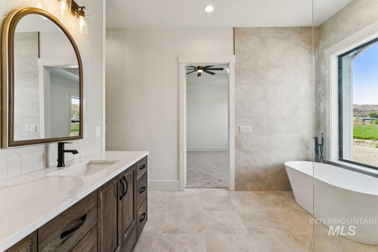 Modern bathroom with a dark wood vanity, arched mirror, marble-look tile, and freestanding tub by a large window.
