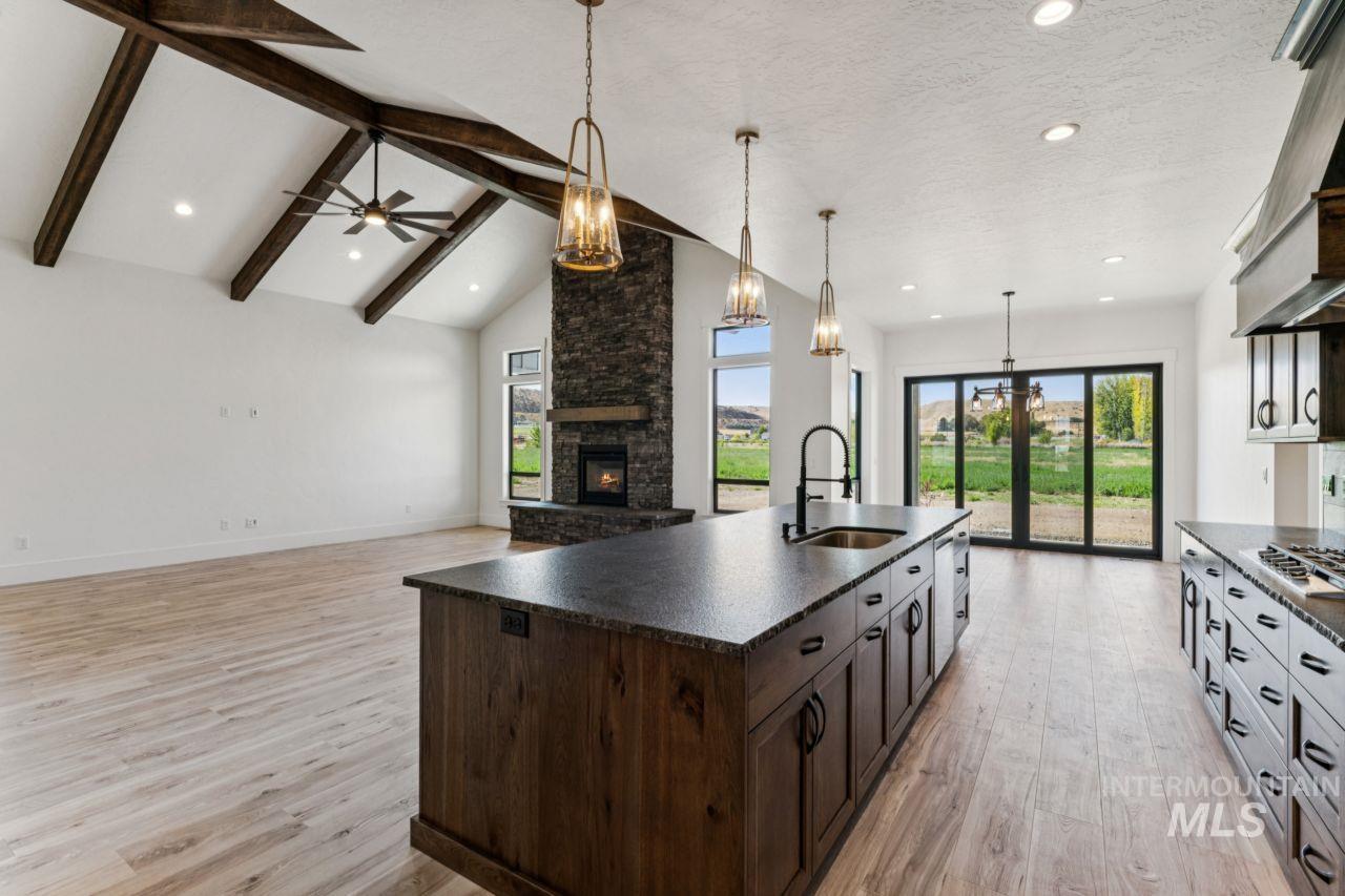 Open kitchen and living area with a large island, exposed ceiling beams, and stone fireplace.